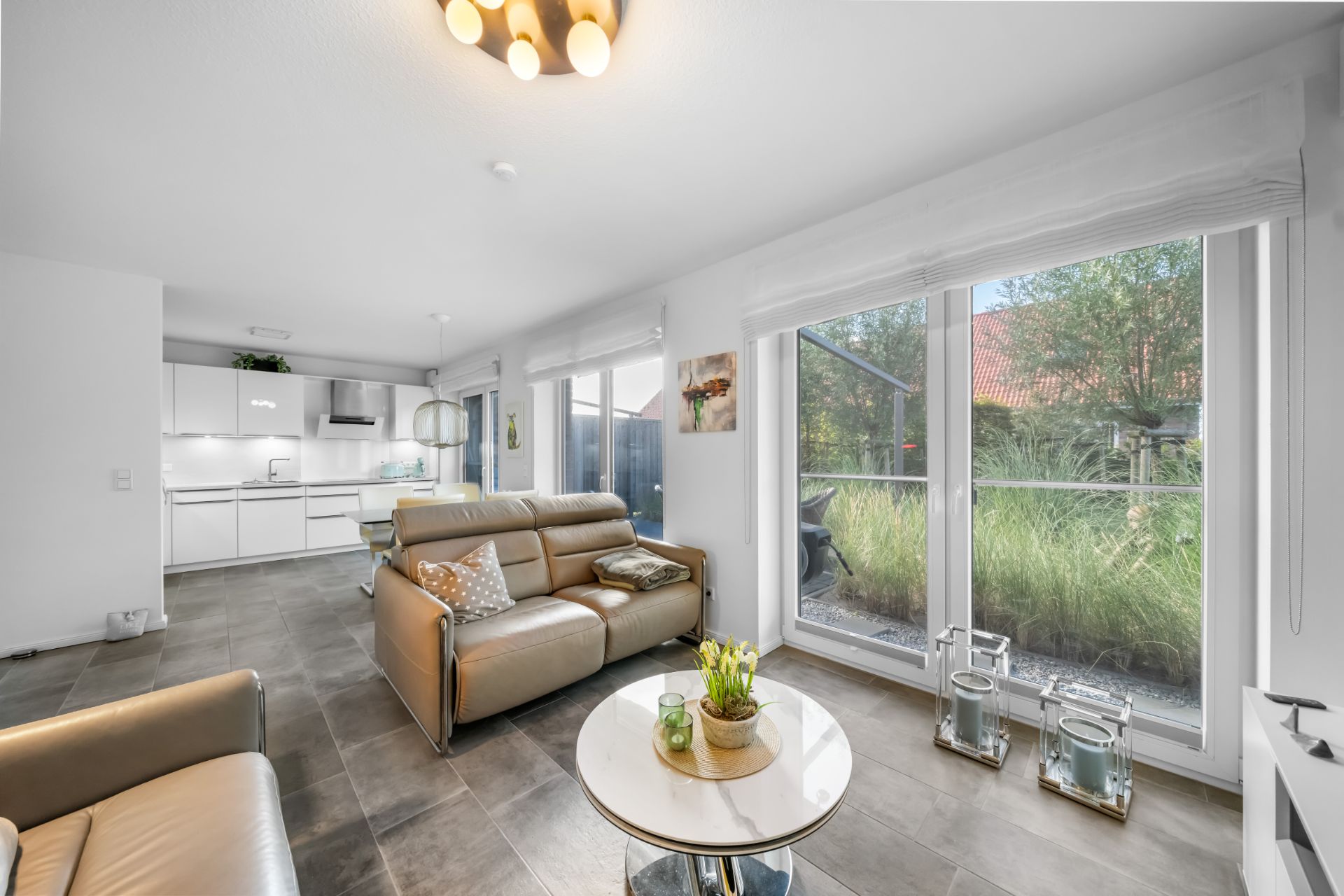 Modernes Wohnzimmer mit Ledersofas, großem Fenster, Couchtisch und Blick in die Küche.