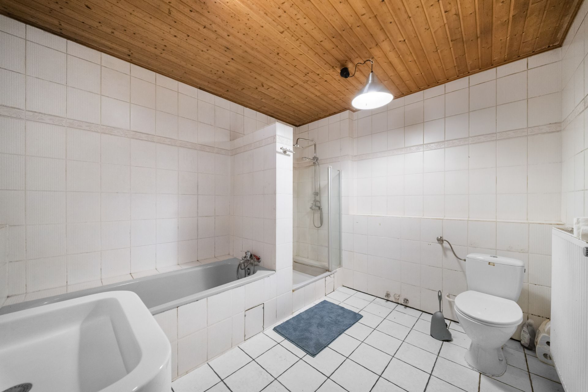 Helles Badezimmer mit Badewanne, Dusche, Toilette und Holzbalkendecke.