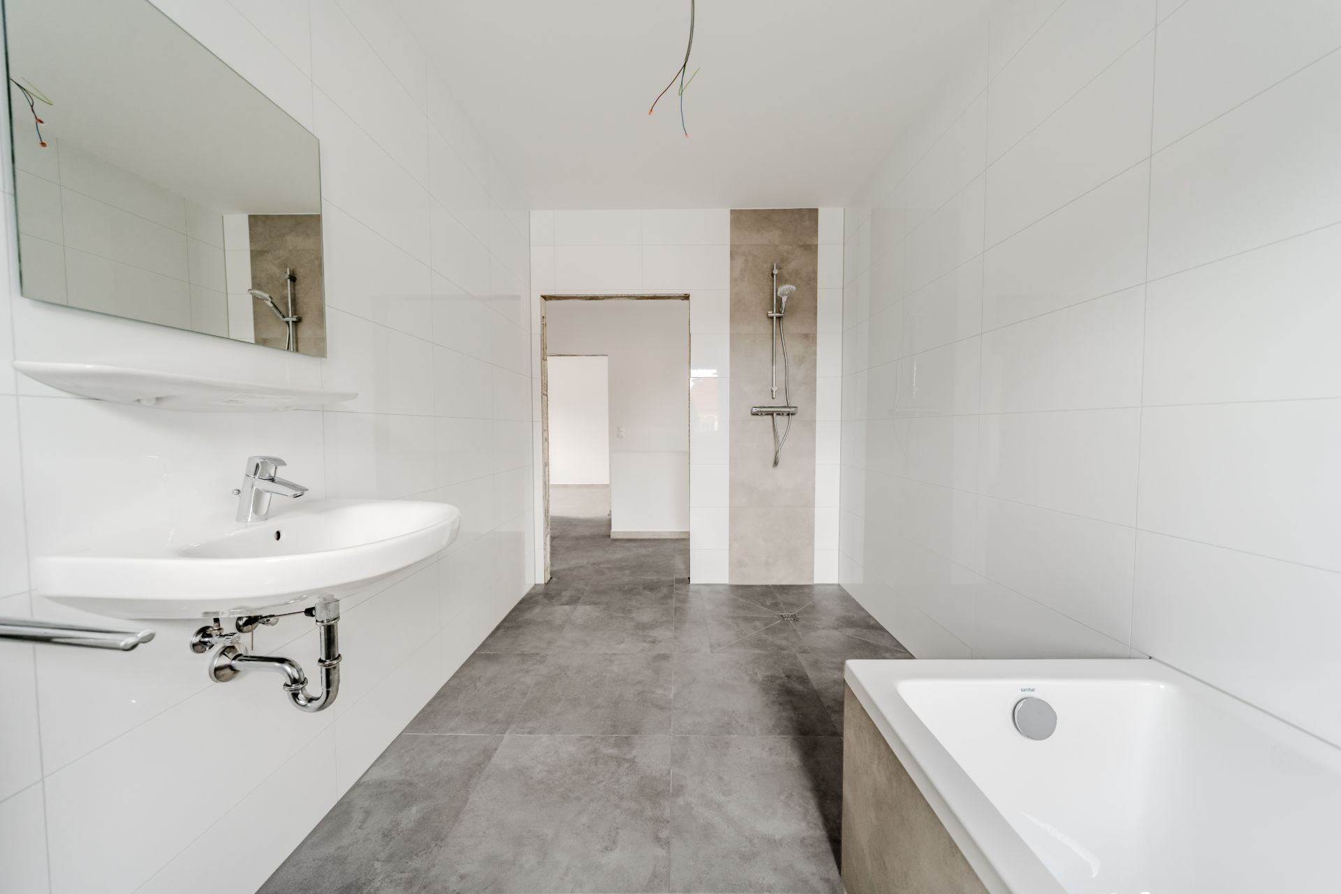 Modernes Badezimmer mit Waschbecken, Spiegel, Badewanne und Dusche auf grauen Fliesen.