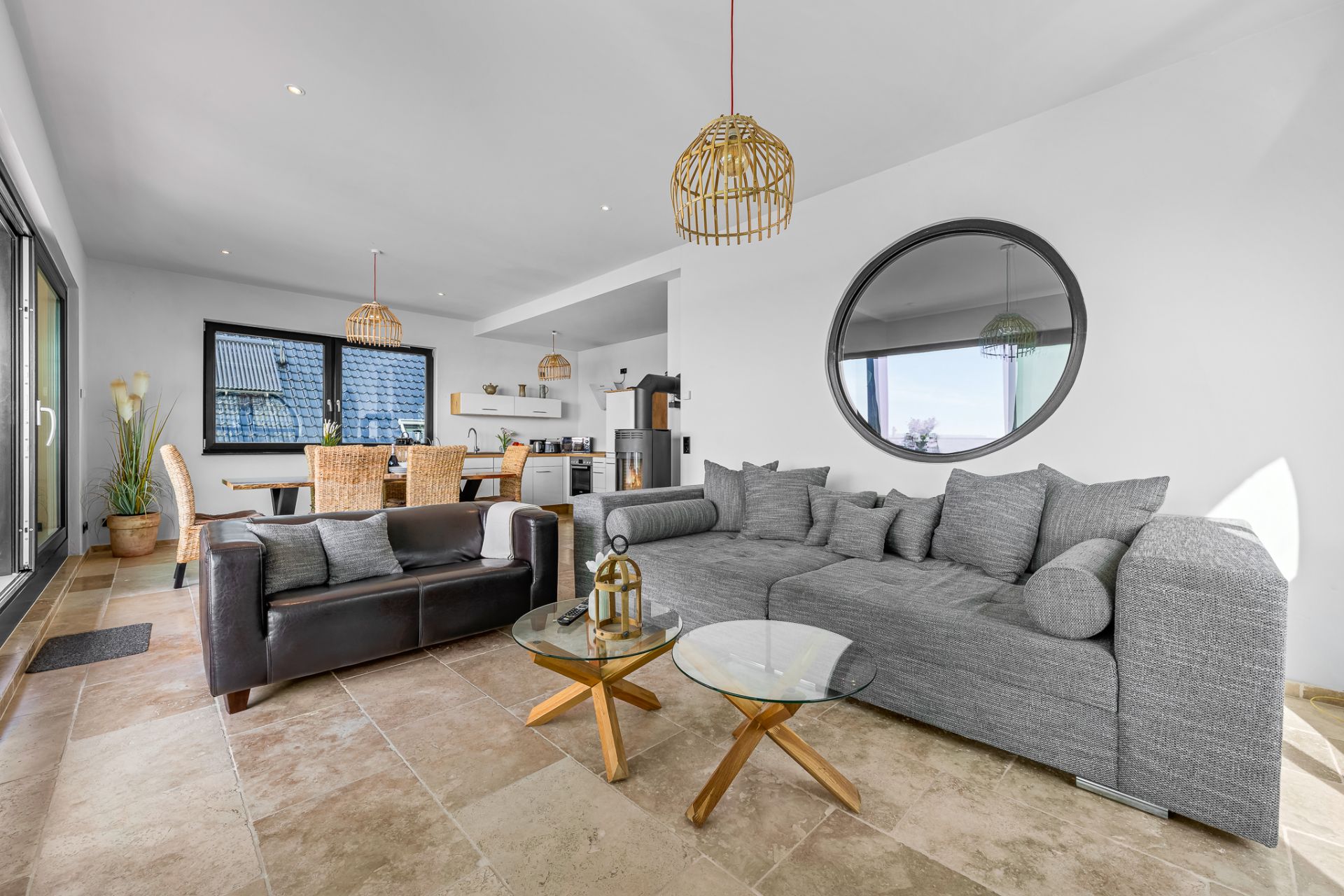Modernes Wohnzimmer mit grauem Sofa, schwarzem Sessel, Glastischen und Essbereich im Hintergrund.