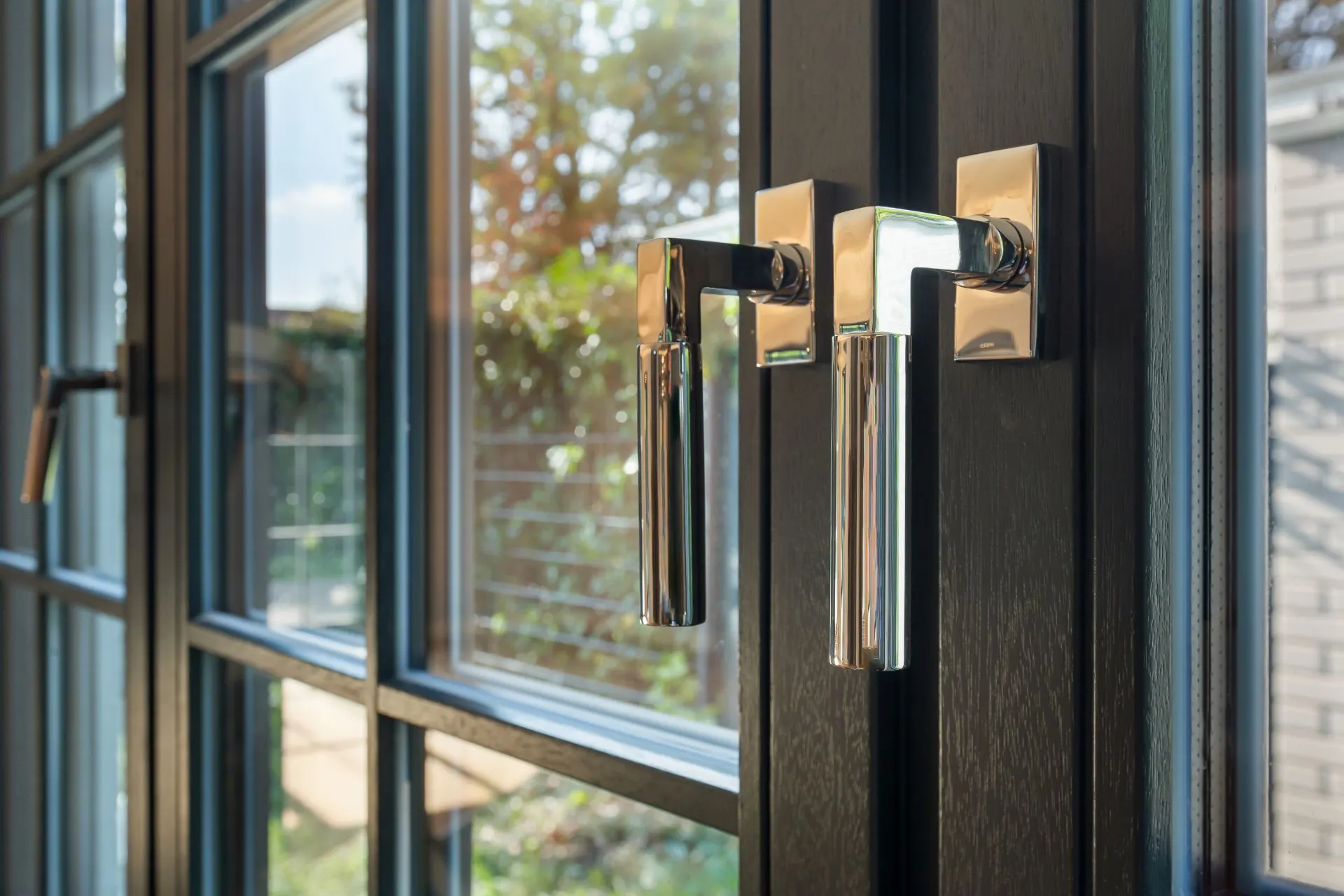 Zwei moderne Fenstergriffe an einem schwarzen Fensterrahmen im Tageslicht.
