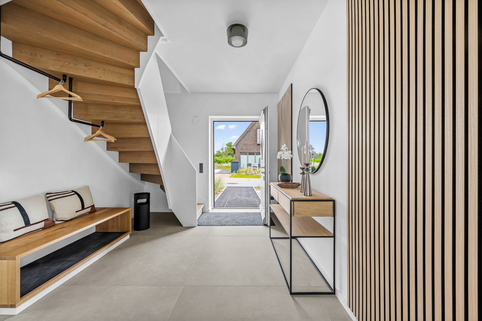 Moderner Flur mit Holztreppe, Bank, Spiegel und Dekoration, offene Haustür mit Blick nach draußen.