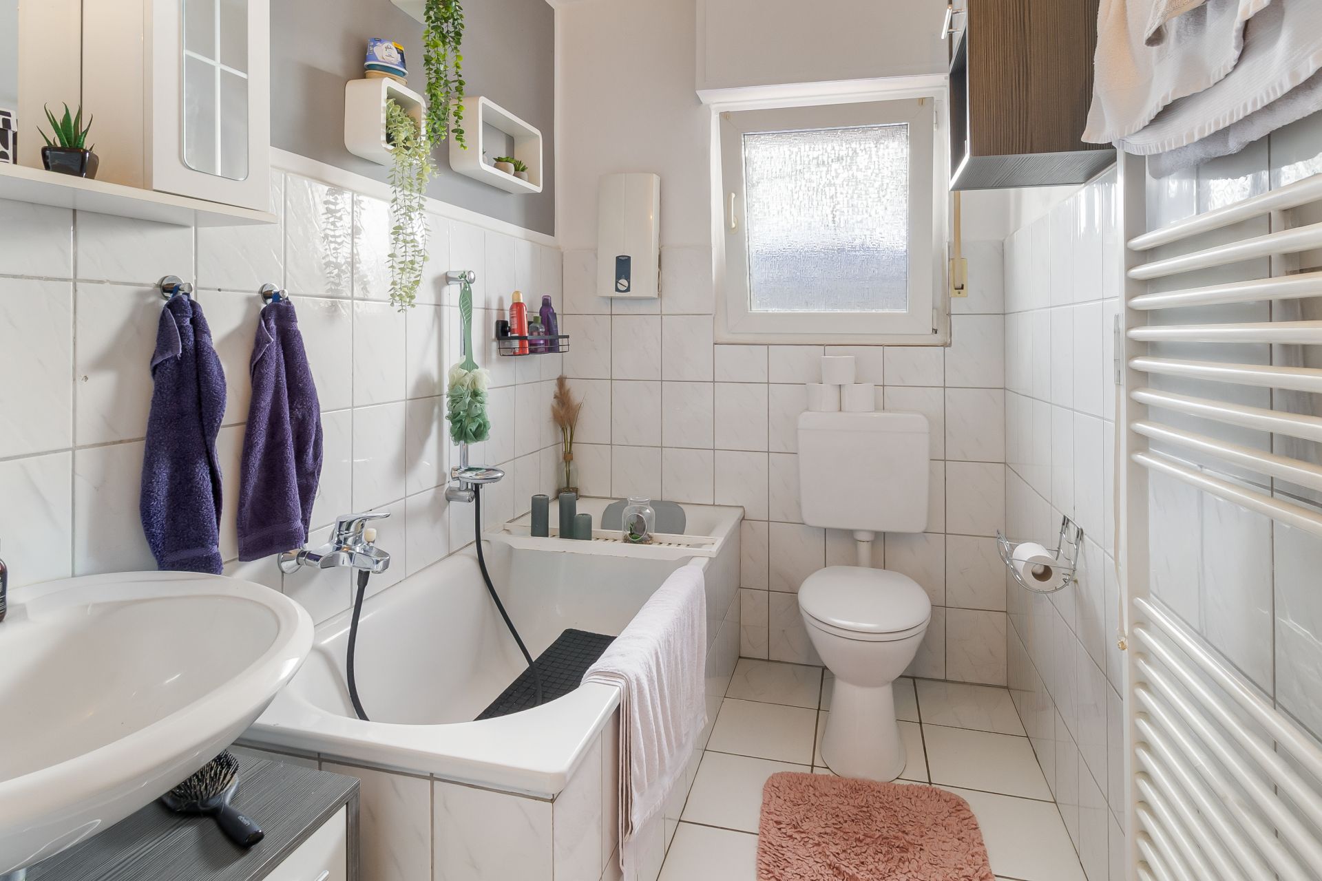Helles Badezimmer mit Badewanne, Waschbecken, WC, Handtüchern und einem Fenster.