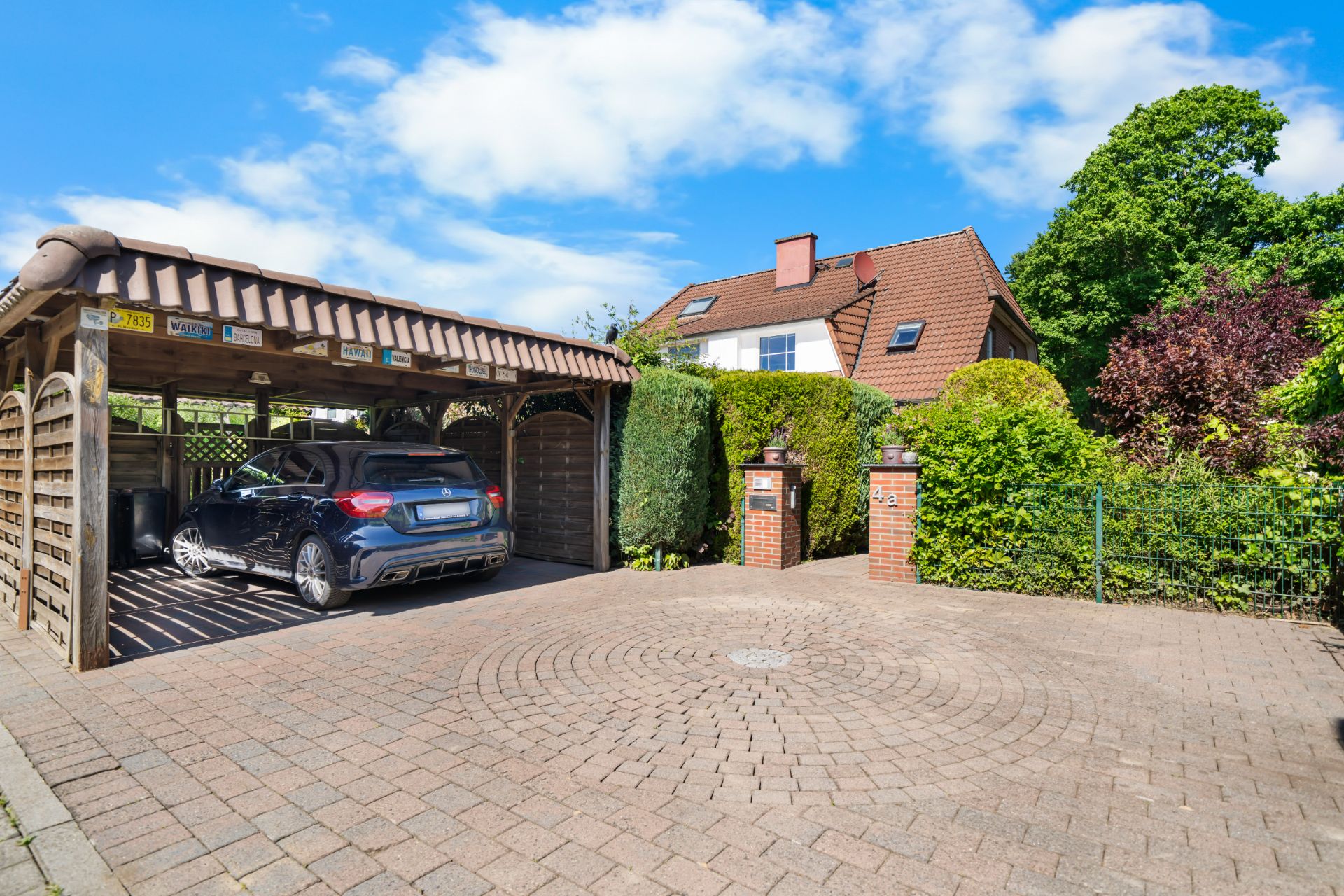 Einfahrt mit Carport und geparktem Auto vor einem Wohnhaus mit rotem Dach.