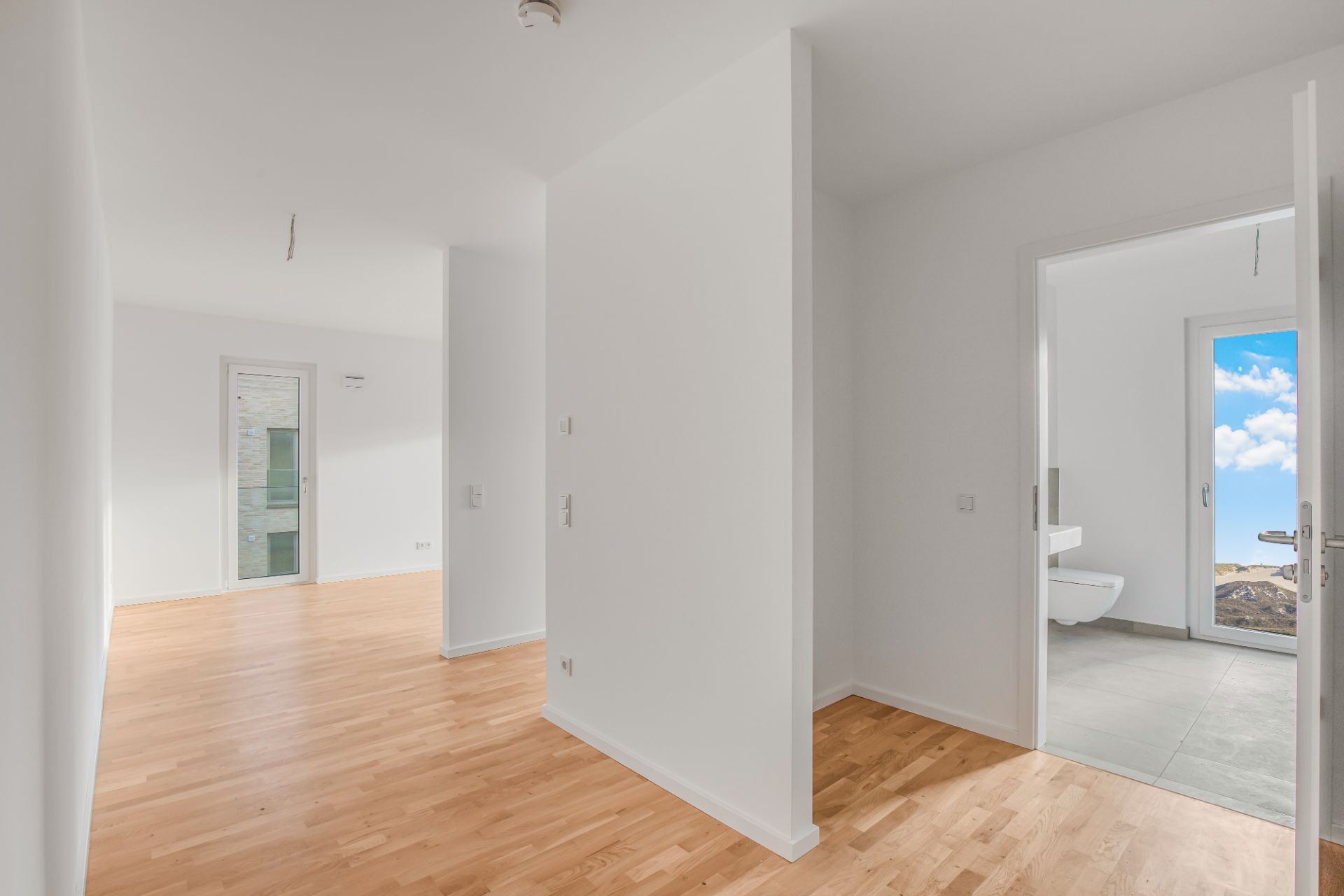 Heller Flur mit Parkettboden, rechts Zugang zu einem Bad mit Fenster und WC.
