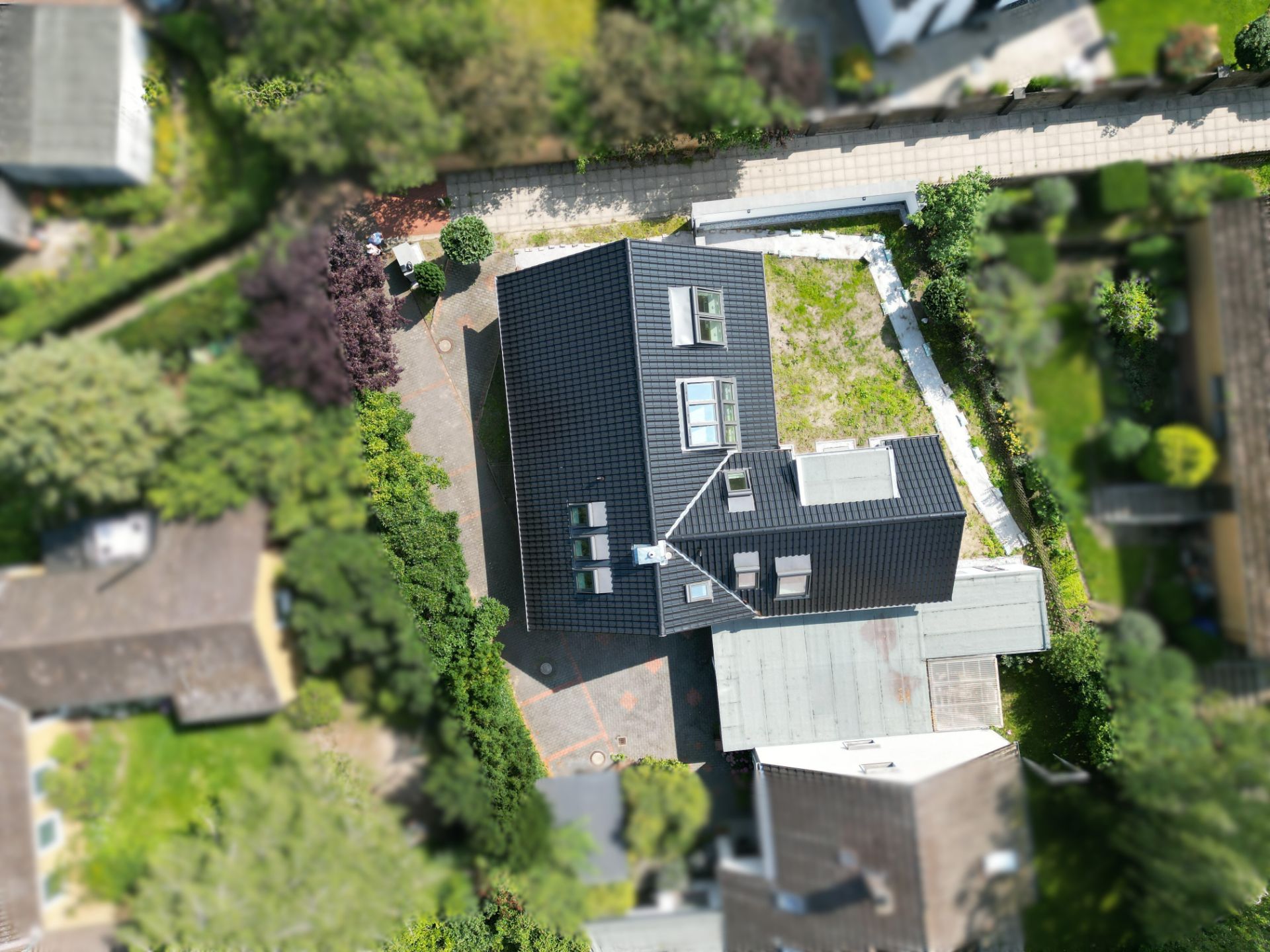 Luftaufnahme eines Wohnhauses mit dunklem Dach und umliegendem Garten.
