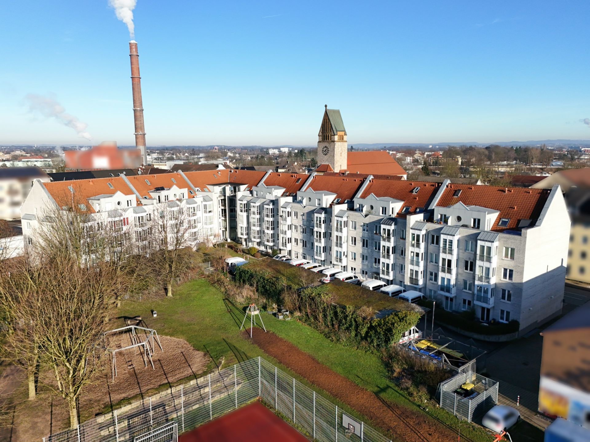 Mehrstöckiges Wohngebäude mit roten Dächern und Spielplatz im Vordergrund bei klarem Himmel.