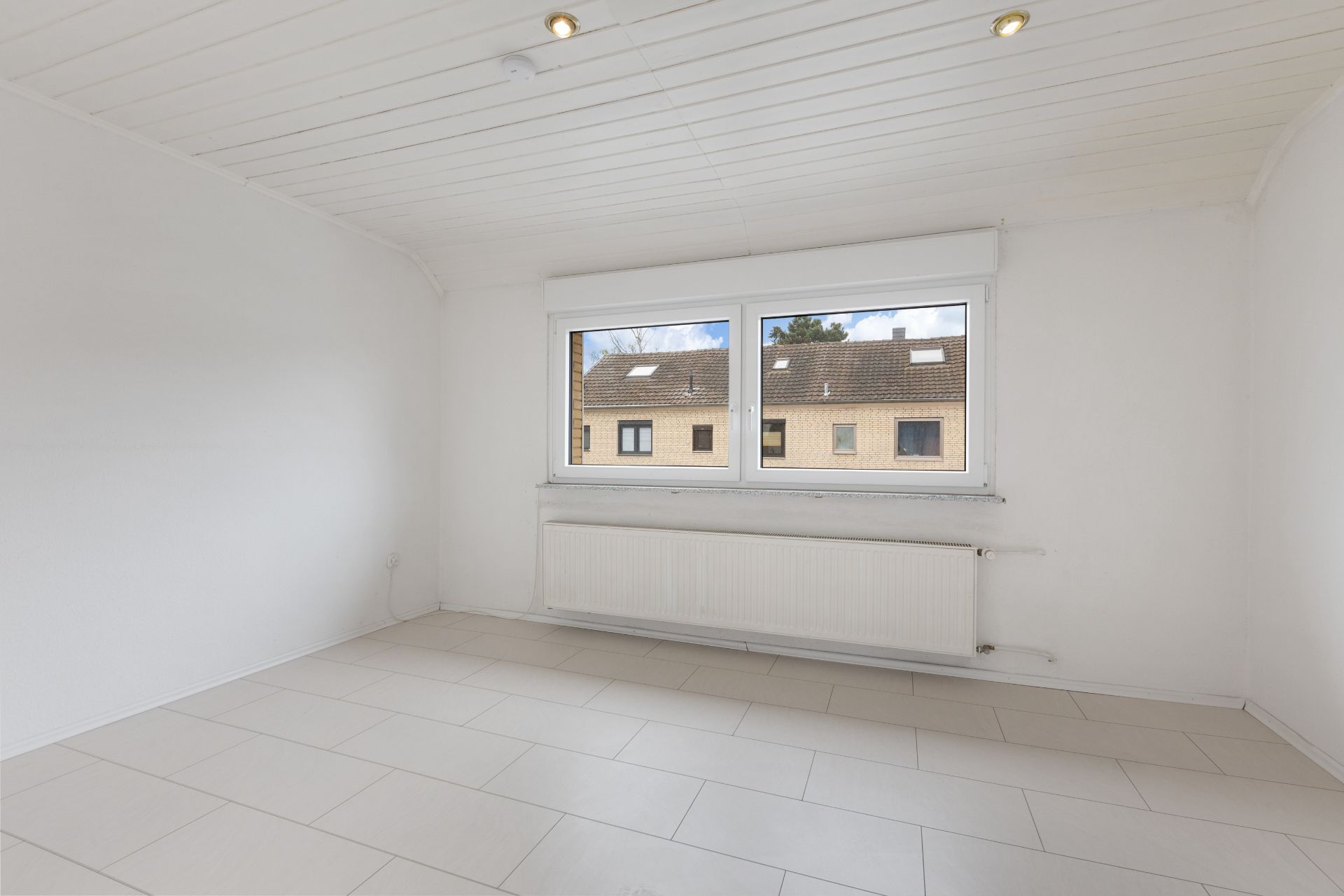 Leerer, heller Raum mit weißen Wänden, Fliesenboden und großem Fenster.