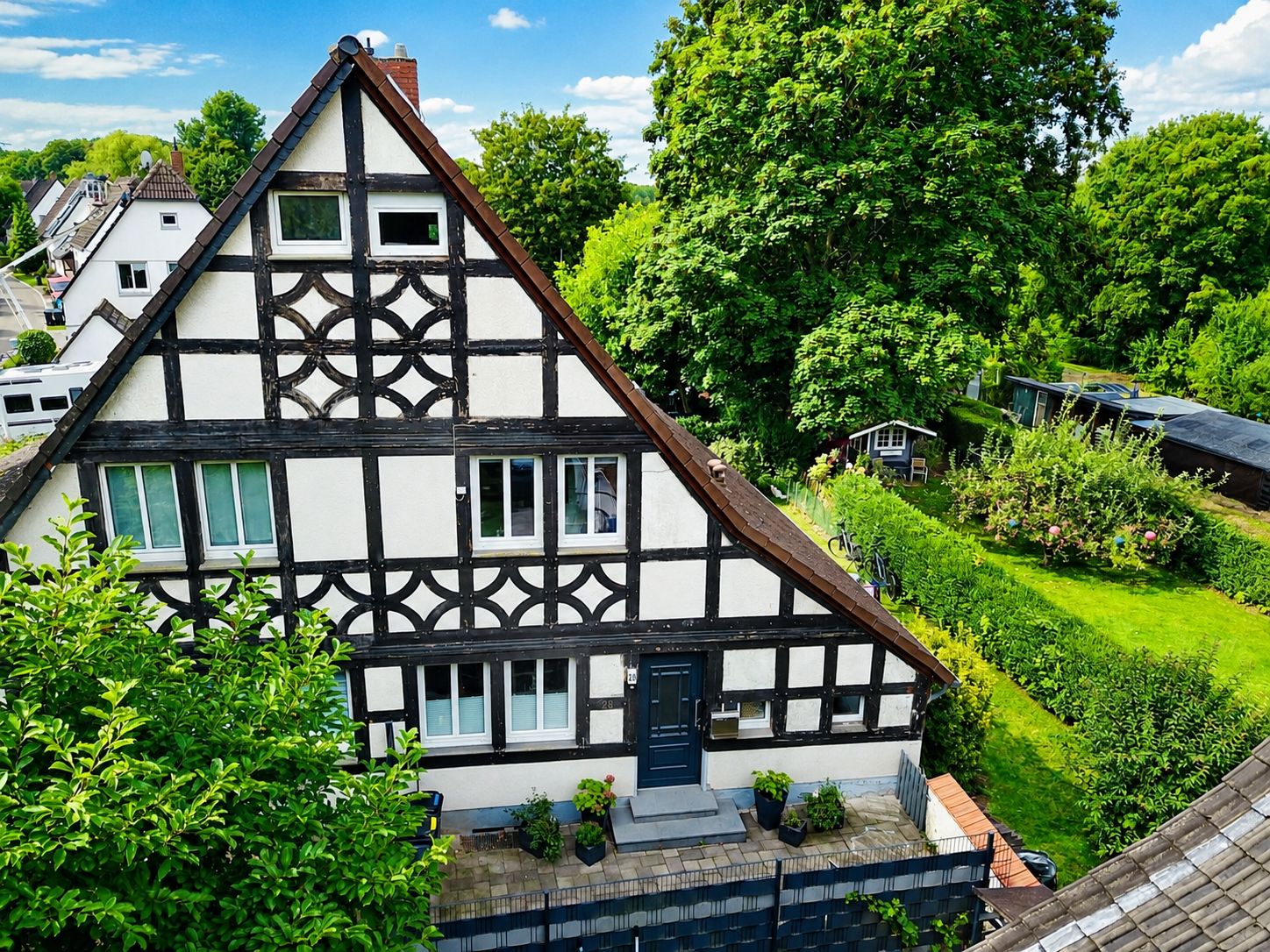 Fachwerkhaus mit Satteldach und großem Garten, umgeben von Bäumen und Pflanzen.