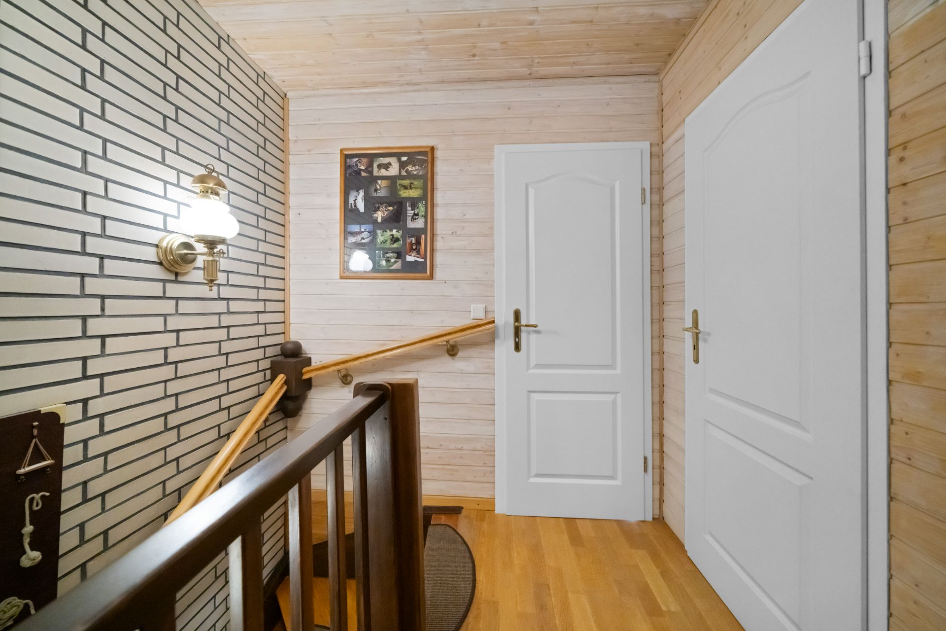 Flur mit Holztreppe, zwei weißen Türen, Holzwänden und gerahmtem Bild an der Wand.