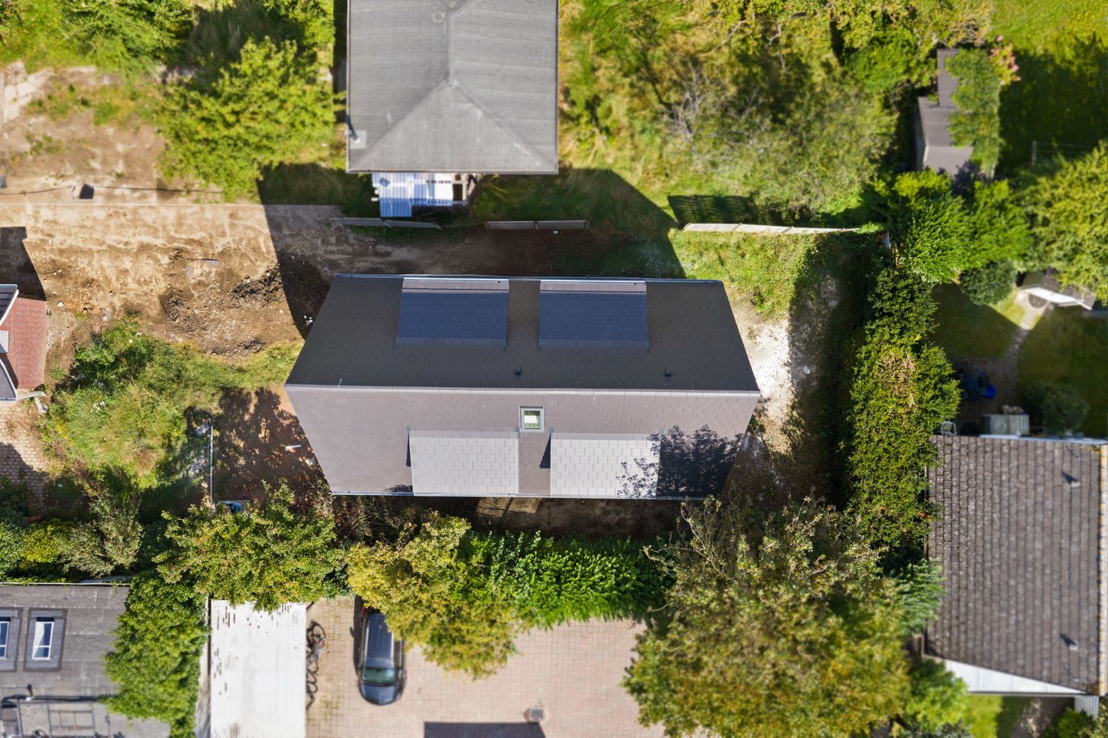 Luftaufnahme eines Hauses mit Solarpanels auf dem Dach, umgeben von Bäumen und Nachbarhäusern.