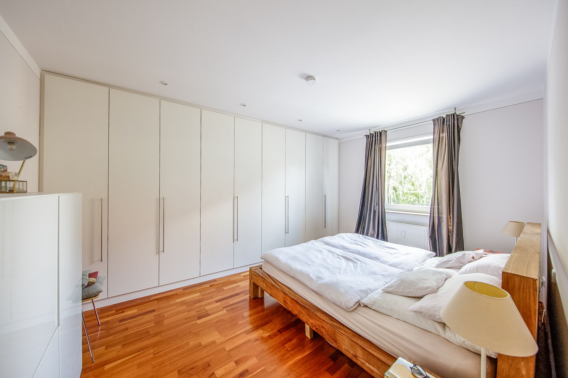 Helles Schlafzimmer mit Holzboden, großem Bett und weißen Einbauschränken.