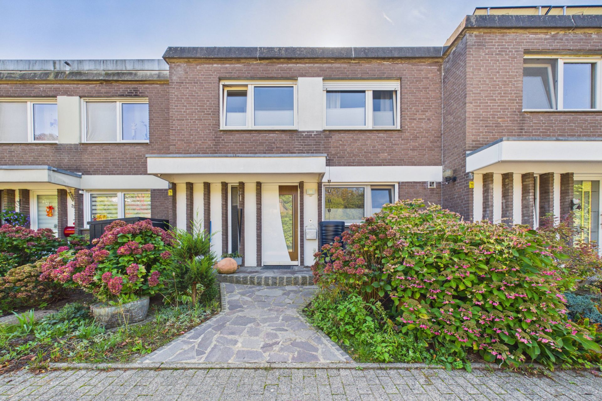 Vorderansicht eines zweistöckigen Reihenhauses mit Blumenbeeten und Gehweg.
