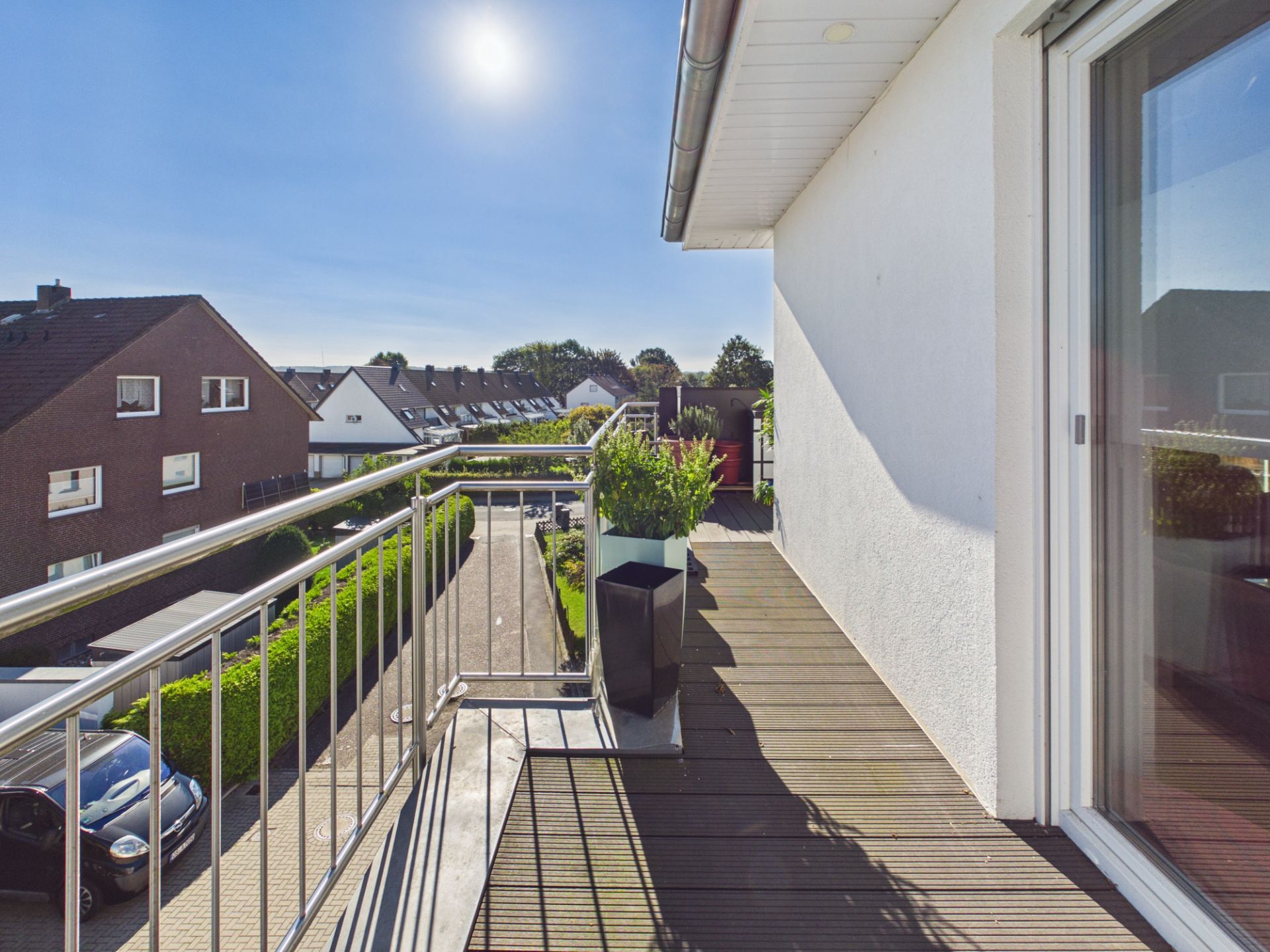 Sonniger Balkon mit Metallgeländer und Pflanzkübeln, Blick auf Wohnhäuser und Straße.