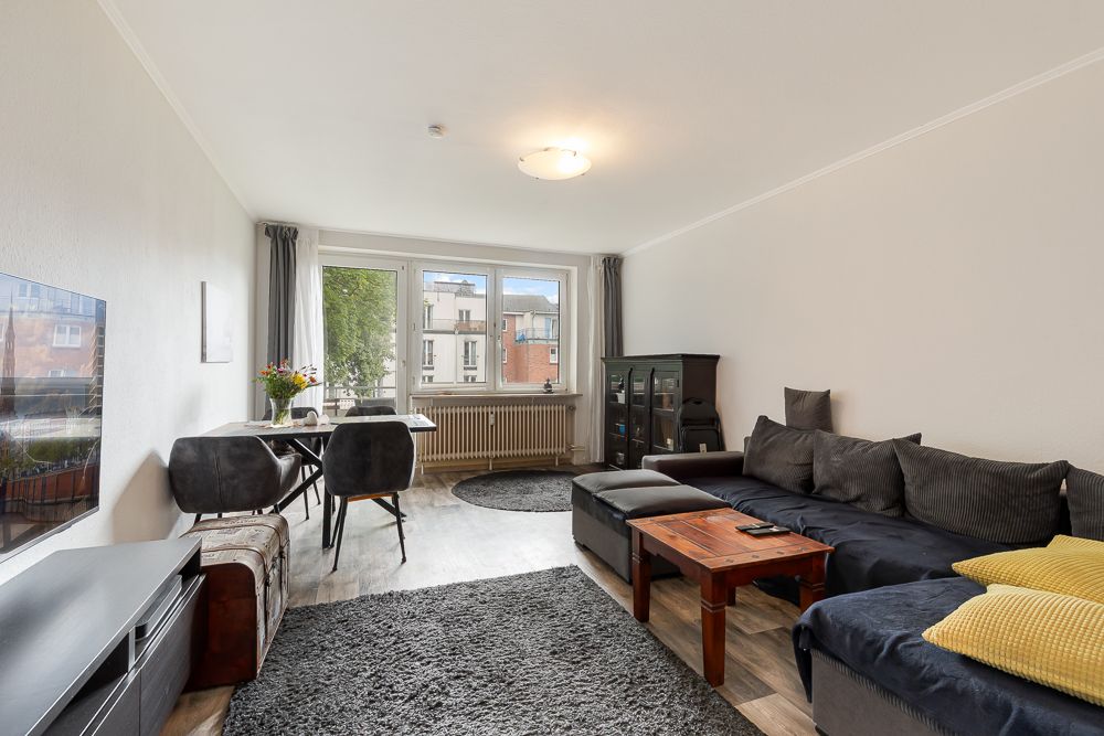 Wohnzimmer mit Ecksofa, Couchtisch, Esstisch und großen Fenstern.