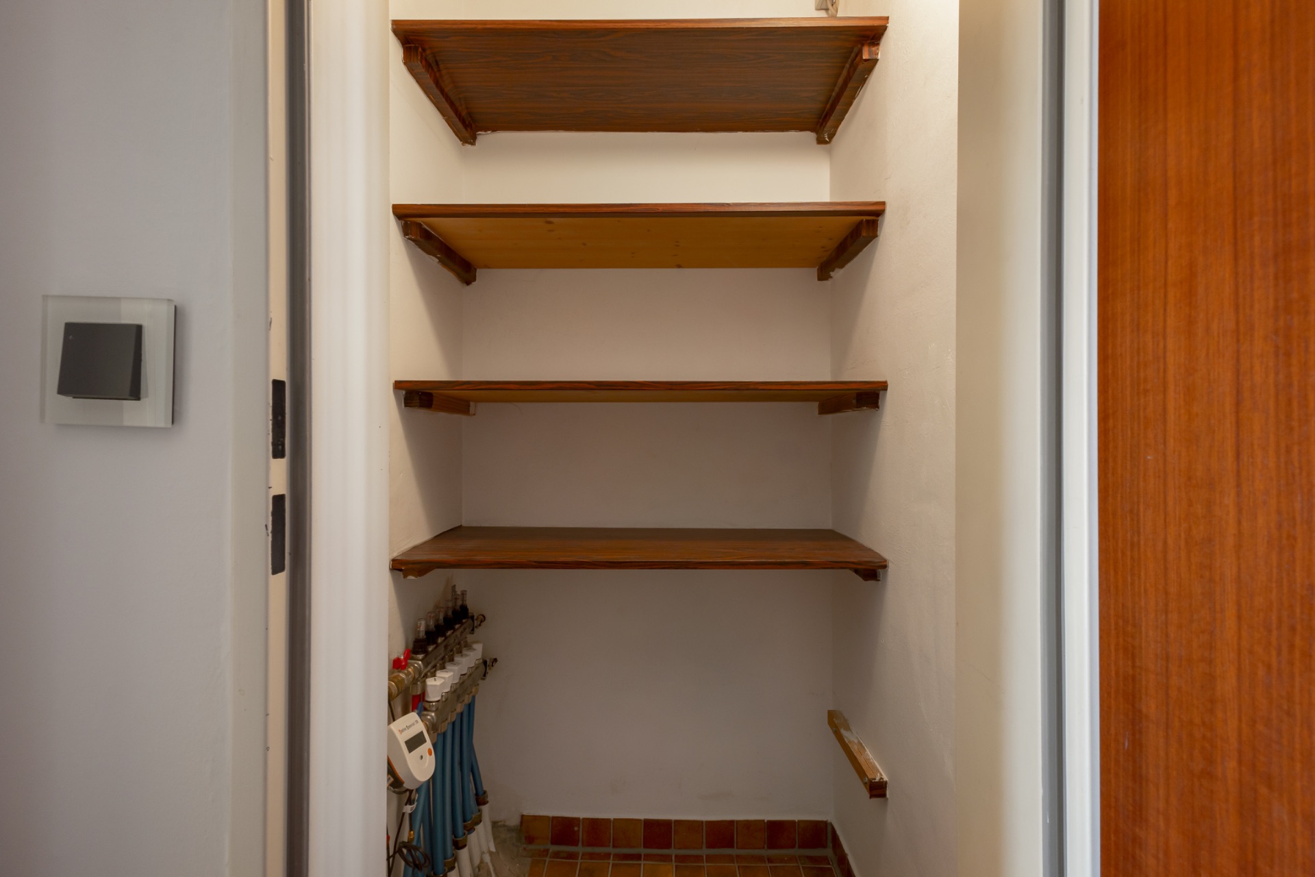 Kleiner Abstellraum mit vier leeren Holzregalen an der Wand.