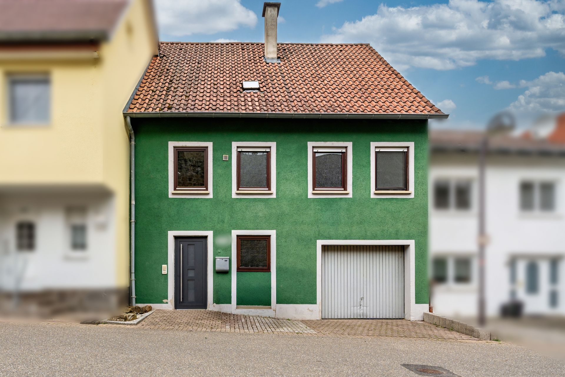 Grünes Wohnhaus mit rotem Ziegeldach, Garage und drei Fenstern in der oberen Etage.