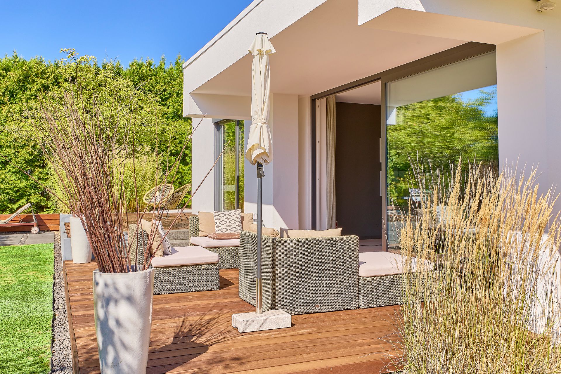 Moderne Terrasse mit Sitzmöbeln, Sonnenschirm und Pflanzen auf Holzdeck vor einem Haus.