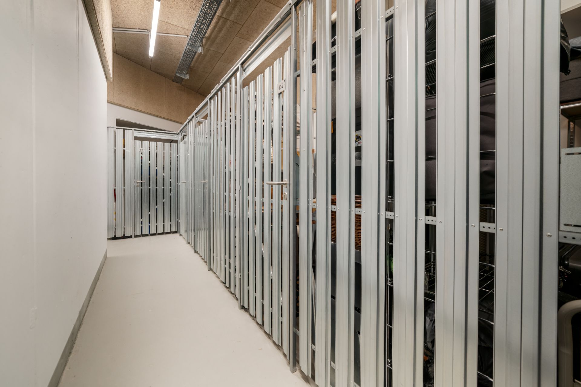 Gang mit mehreren verschlossenen Metallabteilen, vermutlich als Keller oder Lager genutzt.