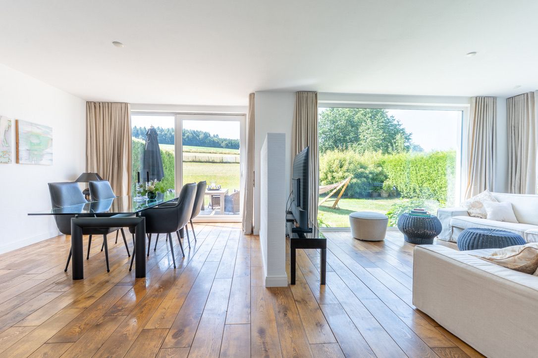 Helles Wohnzimmer mit Sofa, Esstisch und großen Fenstern mit Blick auf den Garten.