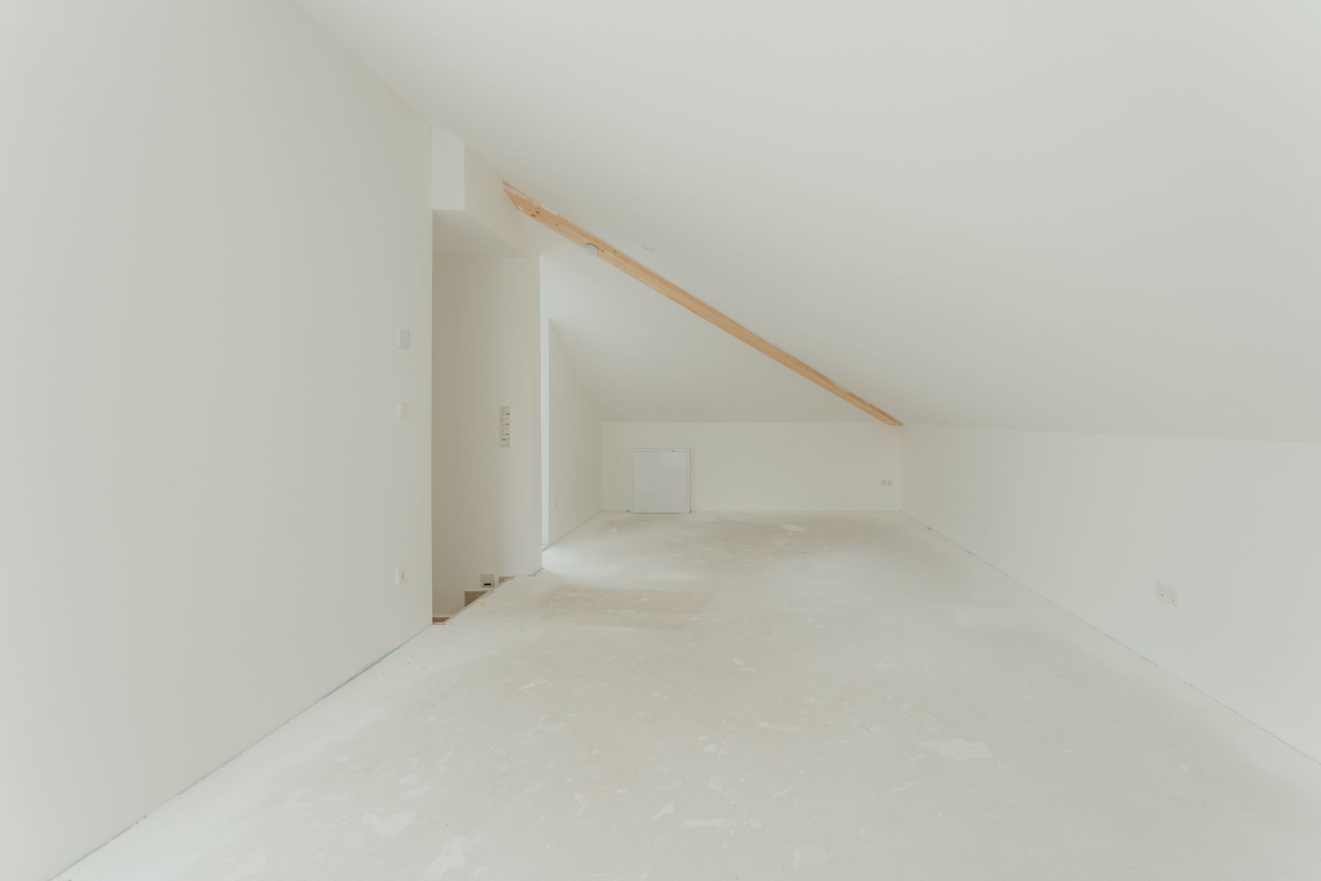 Leerer, weiß gestrichener Dachbodenraum mit schräger Decke und sichtbarem Holzträger.