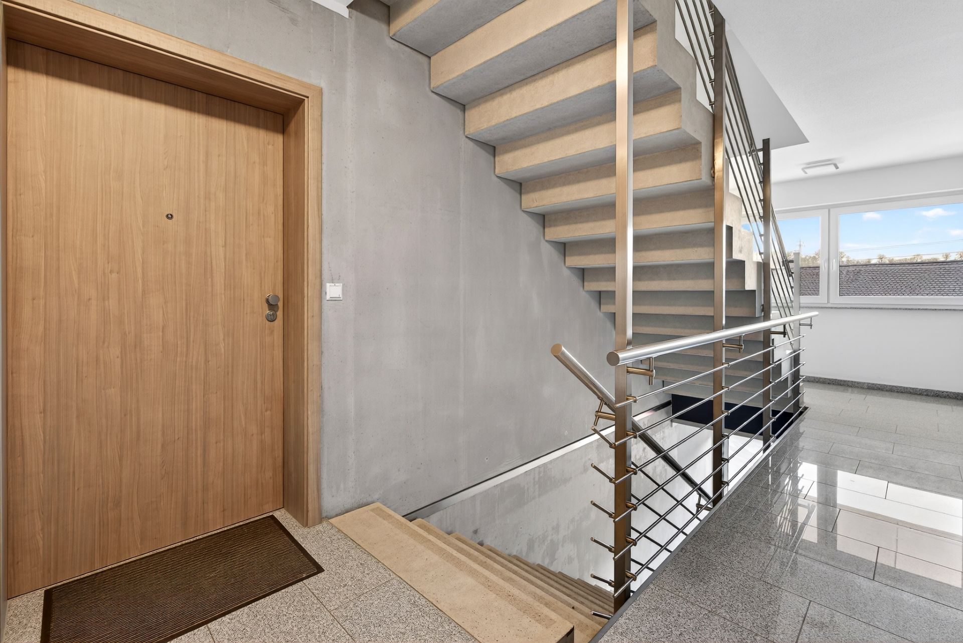 Helles Treppenhaus mit Holztreppen, Metallgeländer und Wohnungstür.