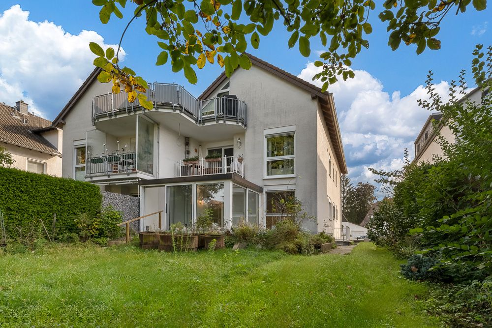 Zweistöckiges Wohnhaus mit Balkonen, Wintergarten und Garten im Vordergrund.