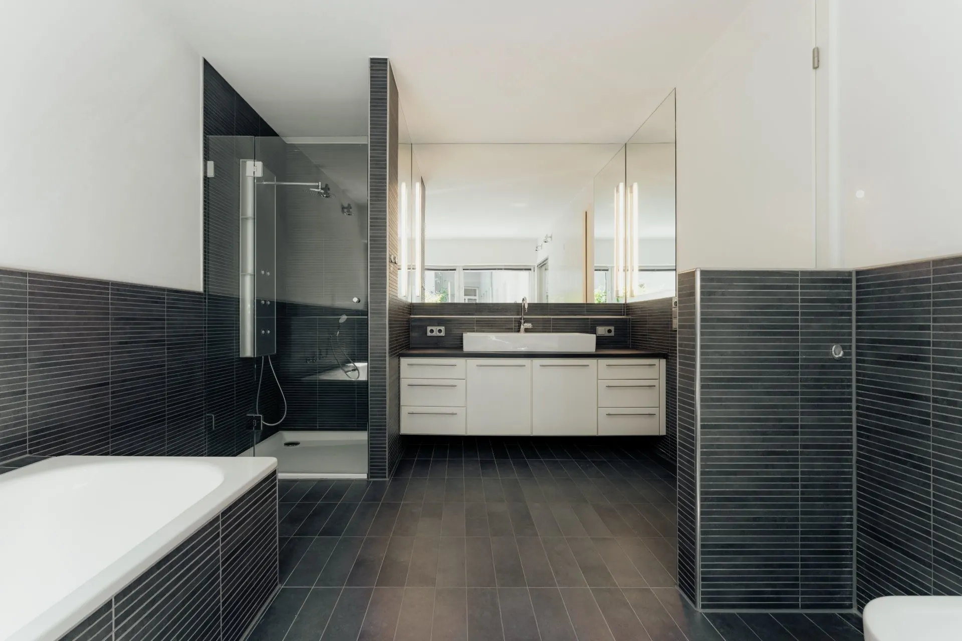 Modernes Badezimmer mit Badewanne, Dusche, großem Spiegel und Waschtisch mit Schränken.