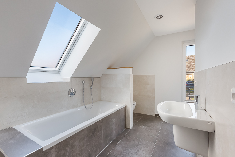 Modernes Badezimmer mit Badewanne, Dachfenster, Waschbecken und Toilette.