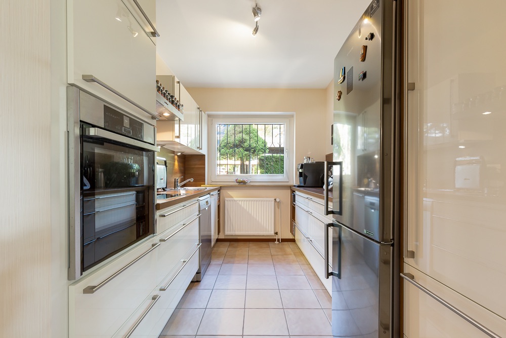 Helle, moderne Küche mit großen Schränken, Backofen, Kühlschrank und Fenster mit Blick ins Grüne.