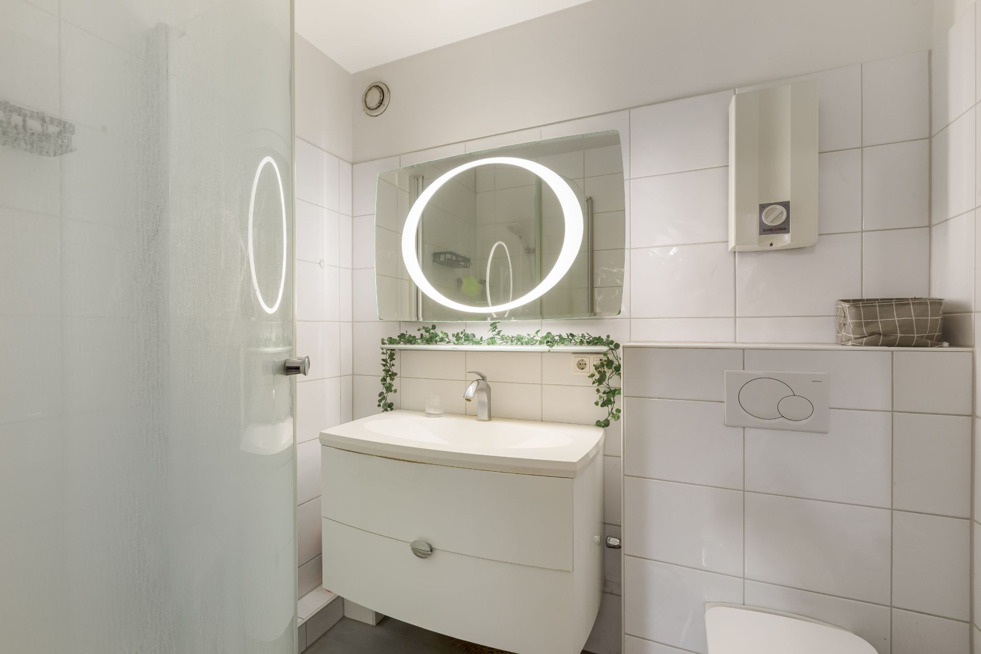 Modernes Badezimmer mit rundem Spiegel, Waschbecken, Dusche und weißen Fliesen.