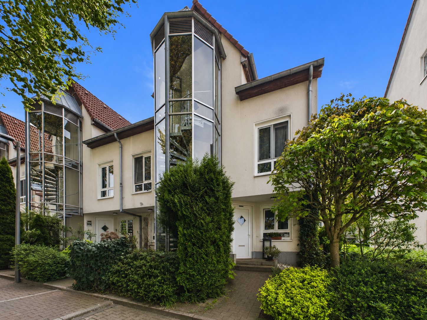 Modernes Reihenhaus mit Glasfassade und viel Grün im Vorgarten.