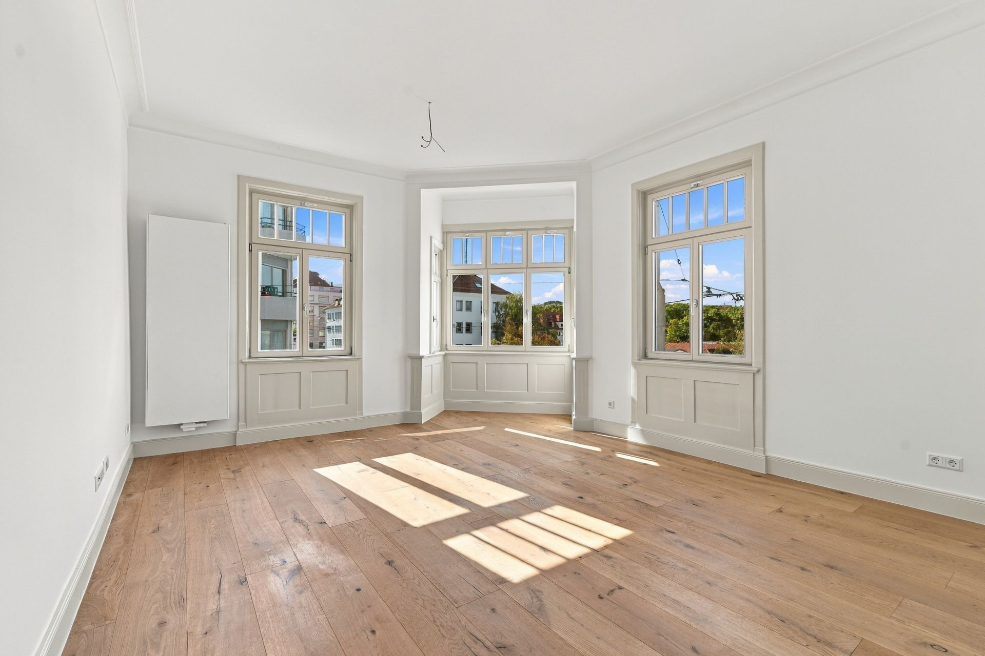 Helles, leeres Zimmer mit Holzboden und drei großen Fenstern.
