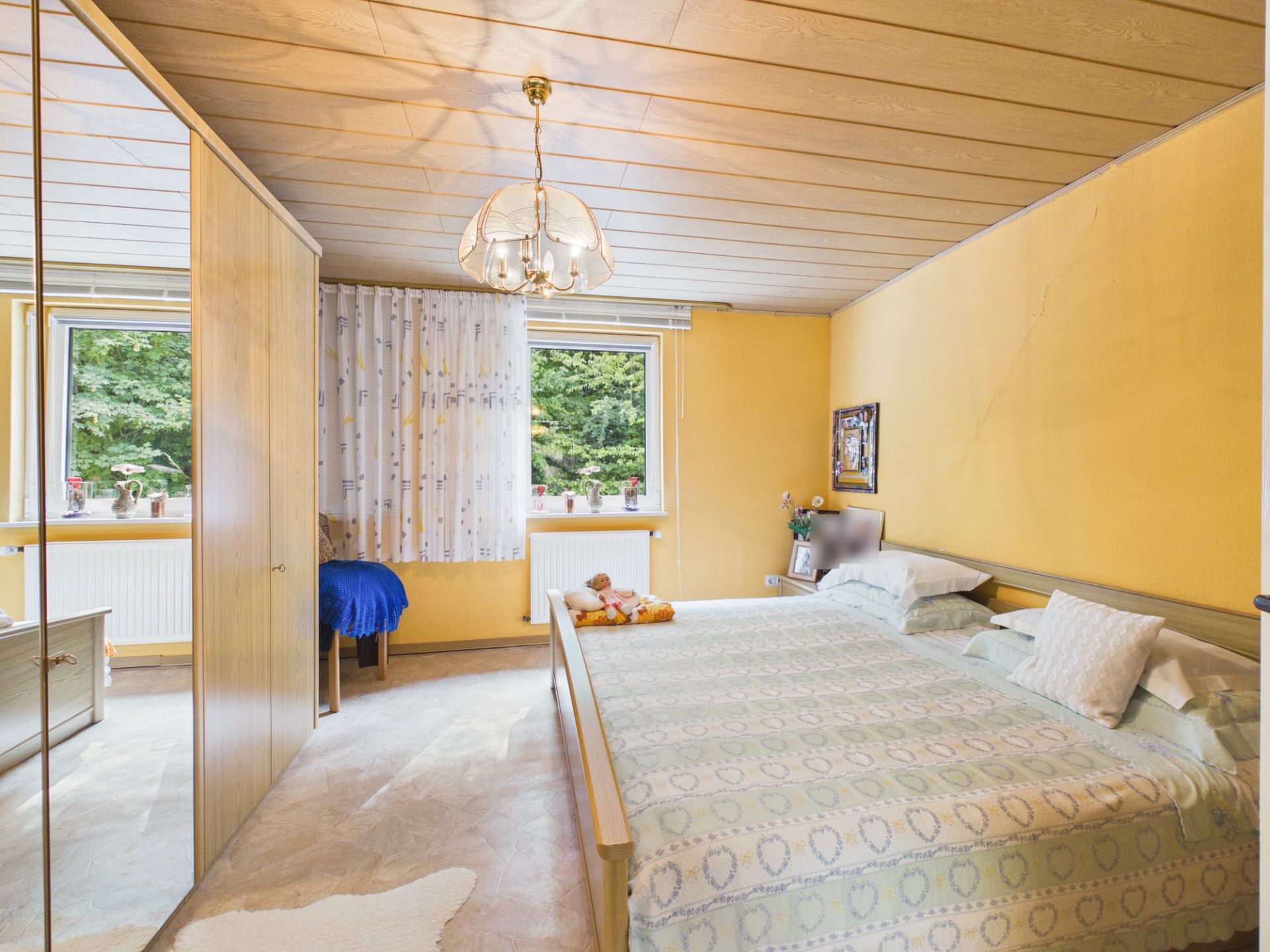 Schlafzimmer mit Doppelbett, gelben Wänden, zwei Fenstern und einem großen Kleiderschrank.