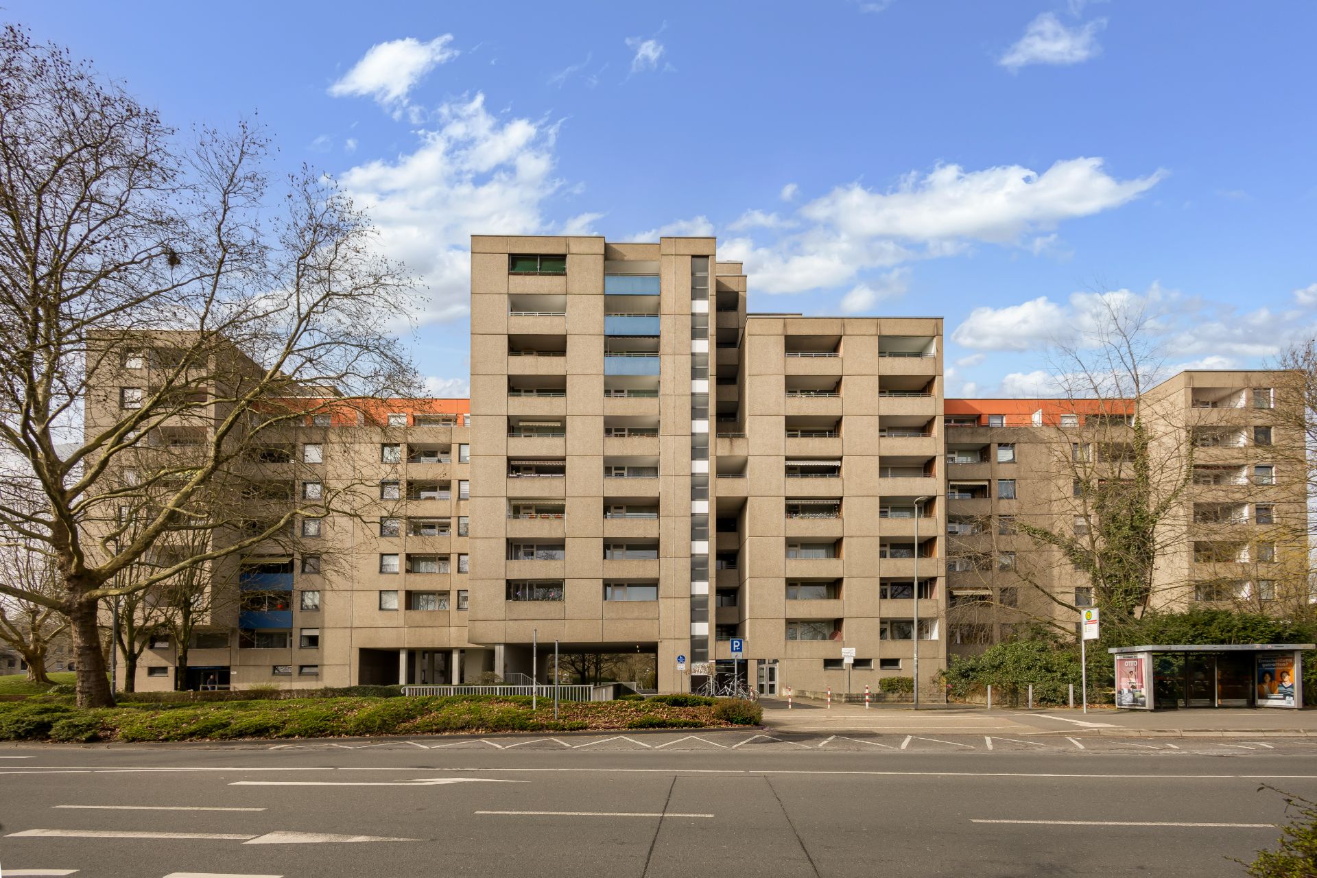 Mehrstöckiges Wohnhaus mit Balkonen und breiter Straße im Vordergrund.