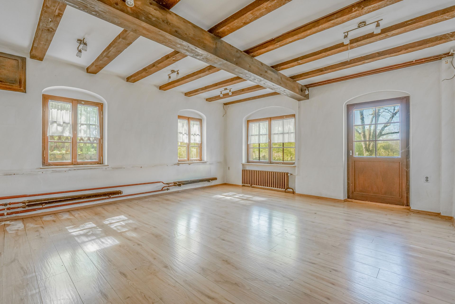 Heller leerer Raum mit Holzboden, sichtbaren Deckenbalken und mehreren Fenstern.