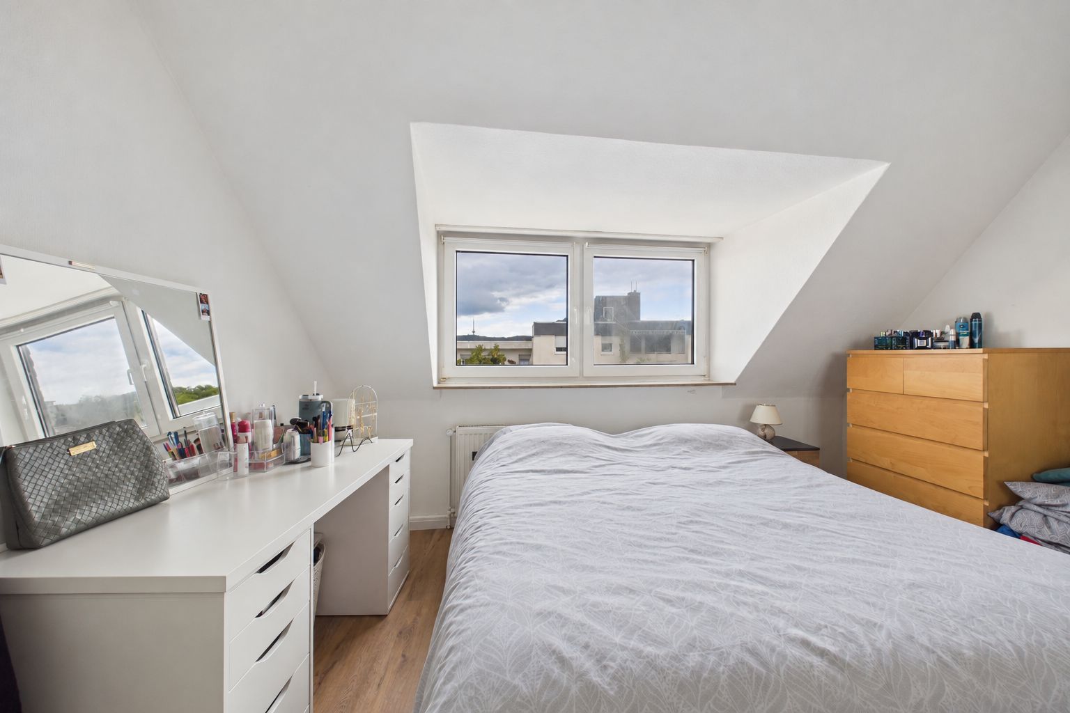 Helles Schlafzimmer mit Bett, Schminktisch, Kommode und Dachfenster.