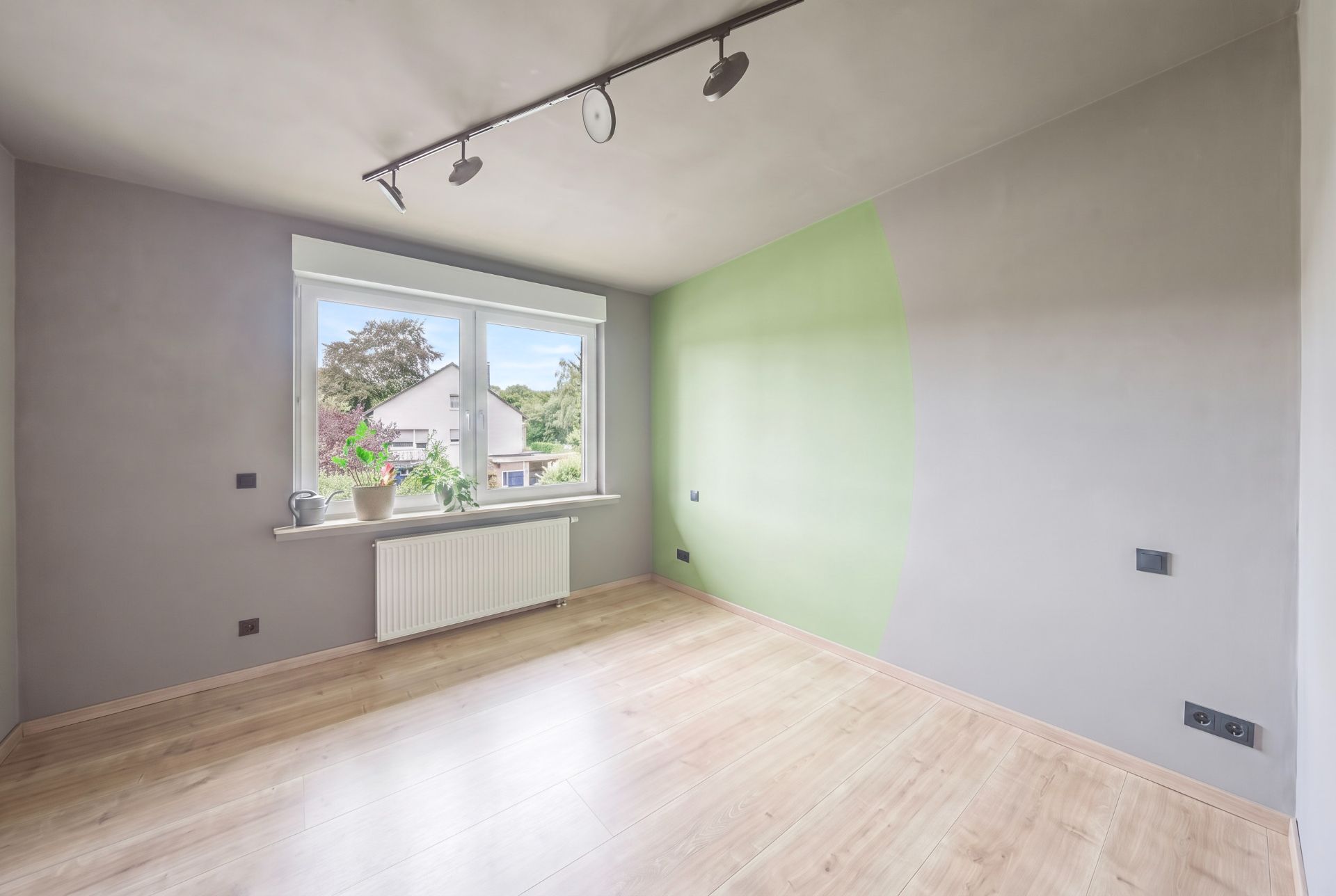 Leerer Raum mit Holzfußboden, großem Fenster, grauen Wänden und grünem Wandabschnitt.