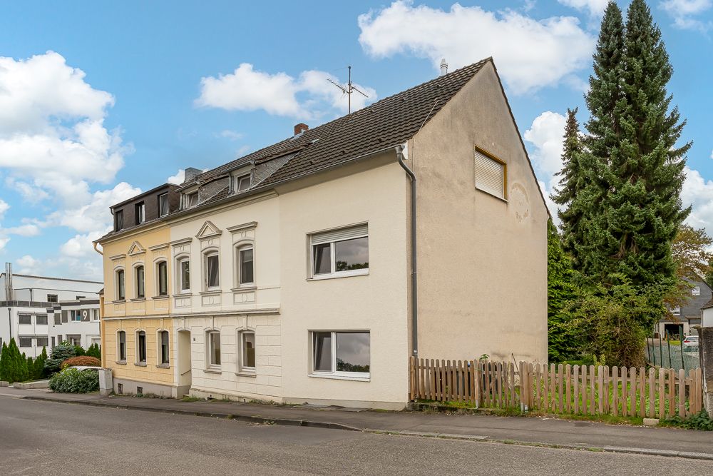 Zweistöckiges Wohnhaus mit heller Fassade, Gartenzaun und Bäumen an der Seite.