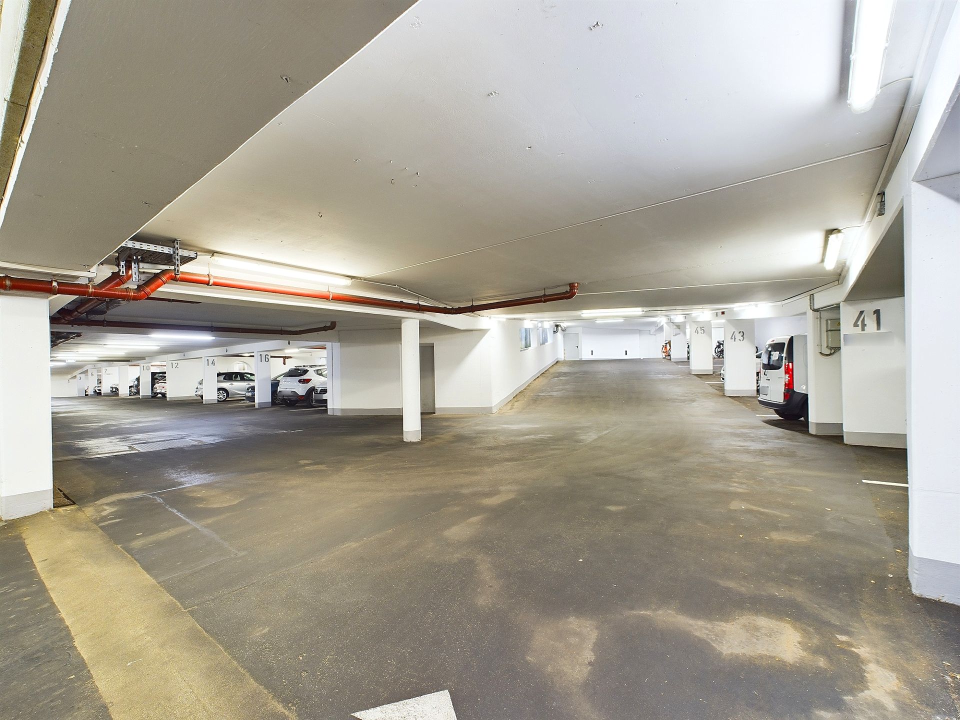 Helle Tiefgarage mit mehreren geparkten Autos und nummerierten Parkplätzen.