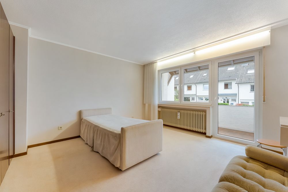 Helles Schlafzimmer mit Einzelbett, großem Fenster und Zugang zu einem Balkon.
