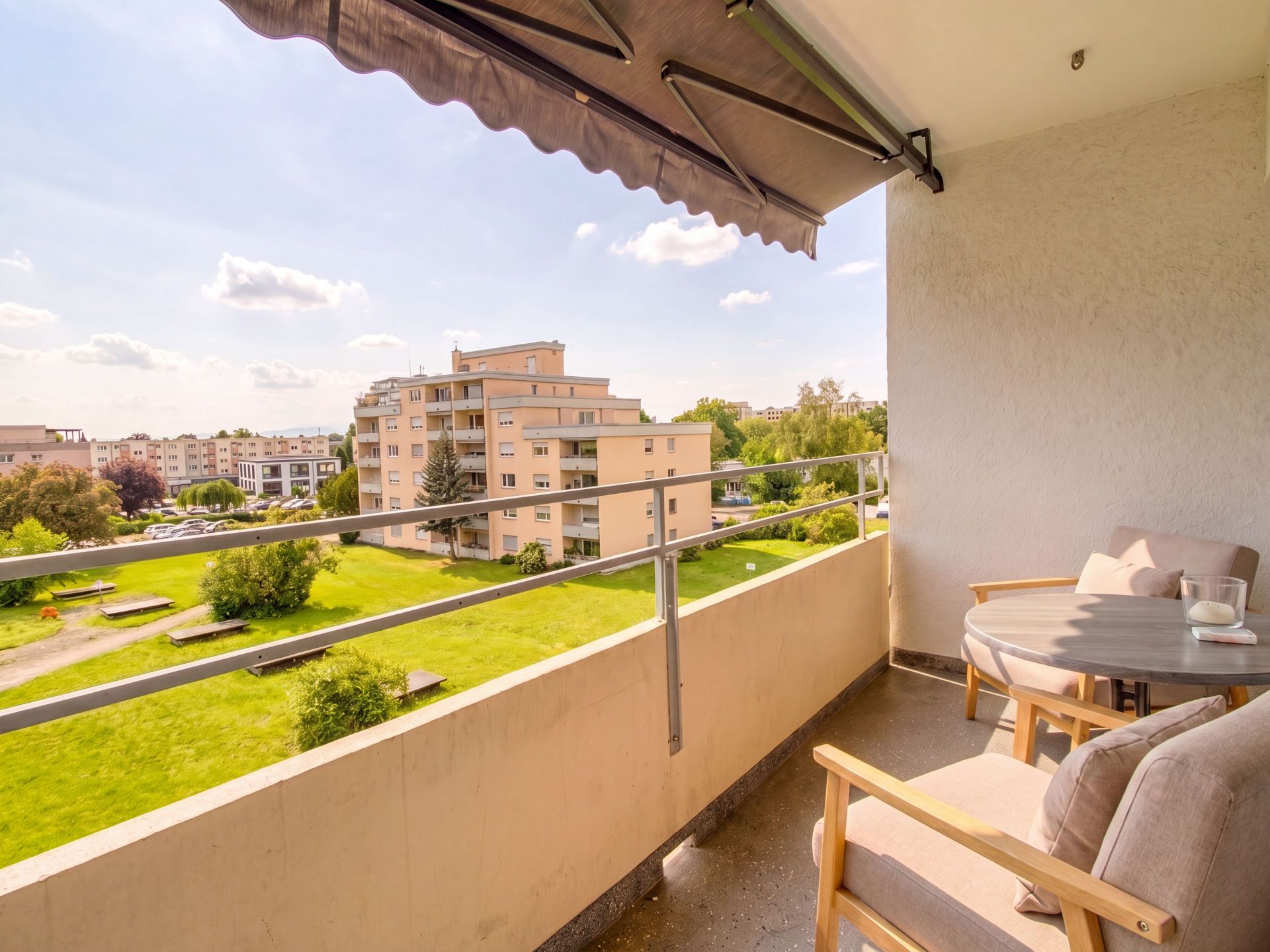 Balkon mit Tisch, zwei Stühlen und Blick auf eine Grünfläche und Wohngebäude.