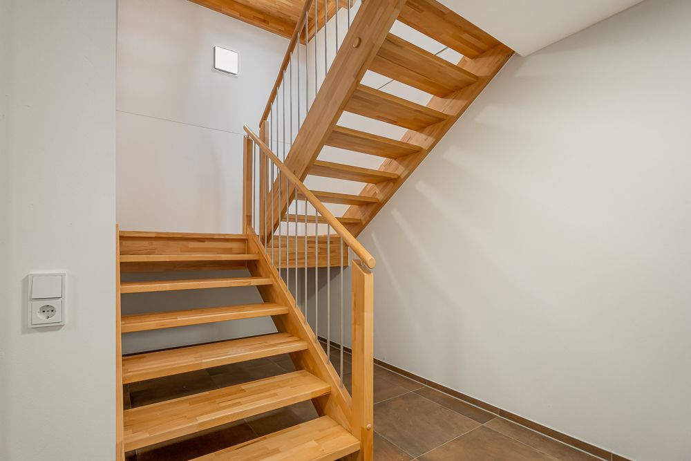 Innenansicht einer modernen Holztreppe mit Handlauf und weißen Wänden.