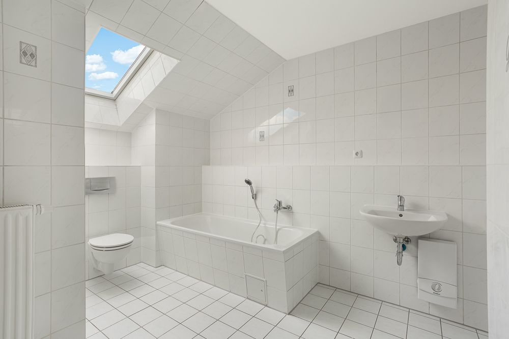 Helles Badezimmer mit Badewanne, WC, Waschbecken und Dachfenster unter Schräge.