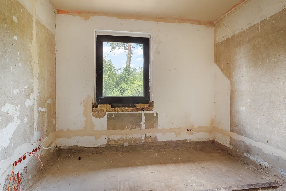 Leerer Raum mit unfertigen Wänden und großem Fenster mit Blick ins Grüne.