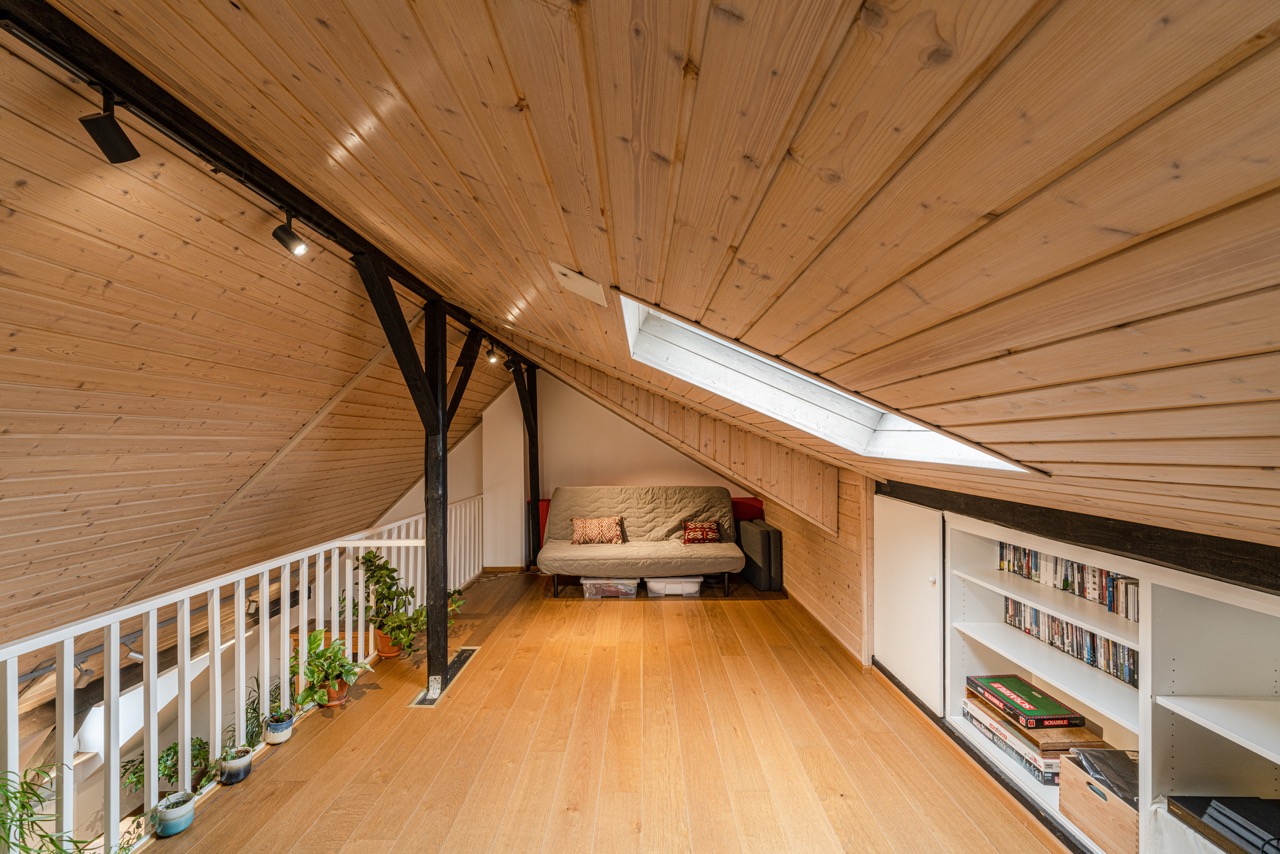 Gemütlicher Dachbodenraum mit Holzdecke, Sofa, Pflanzen, Bücherregal und Dachfenster.