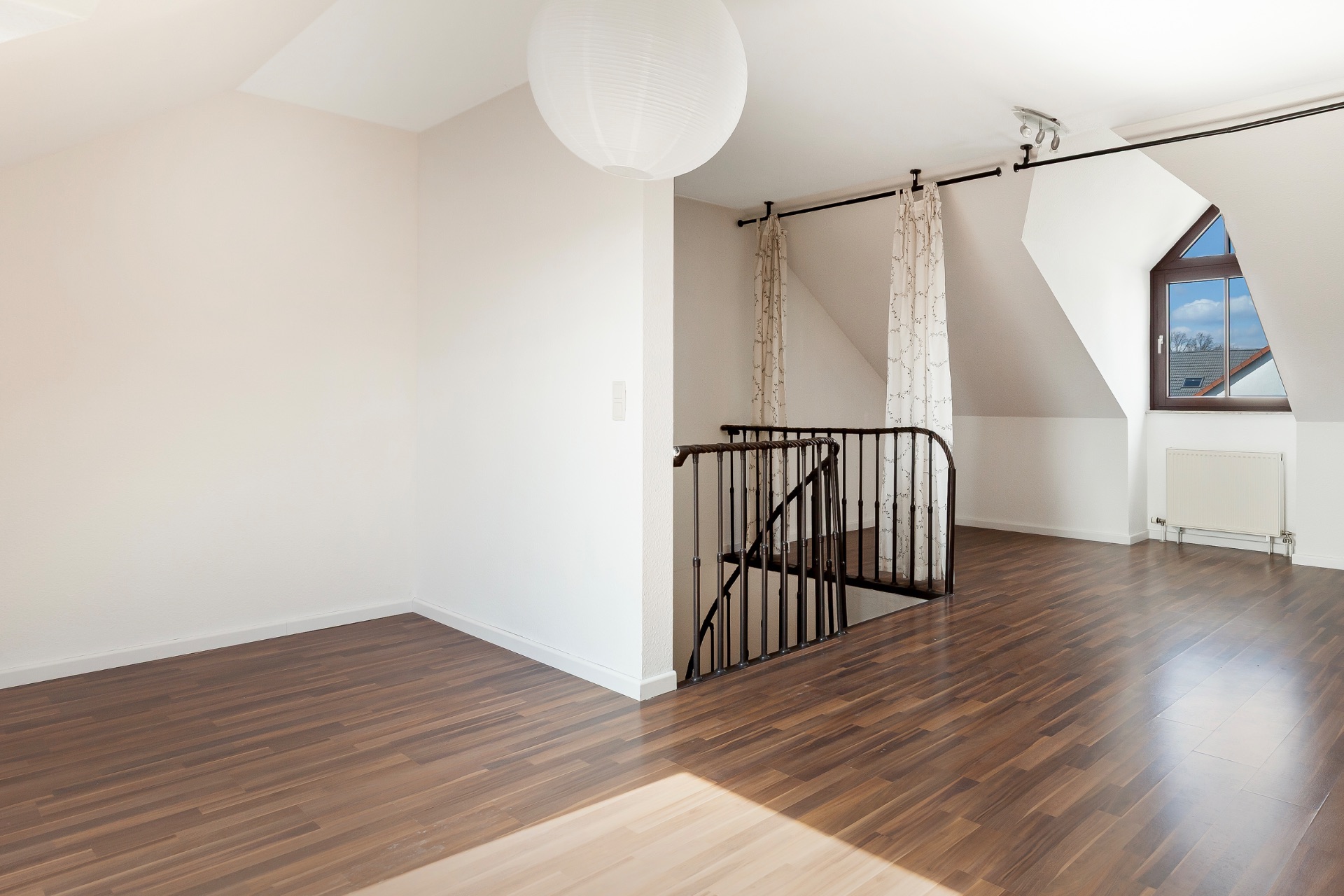 Heller Dachgeschossraum mit Holzfußboden, Treppe, Fenster und Vorhängen.