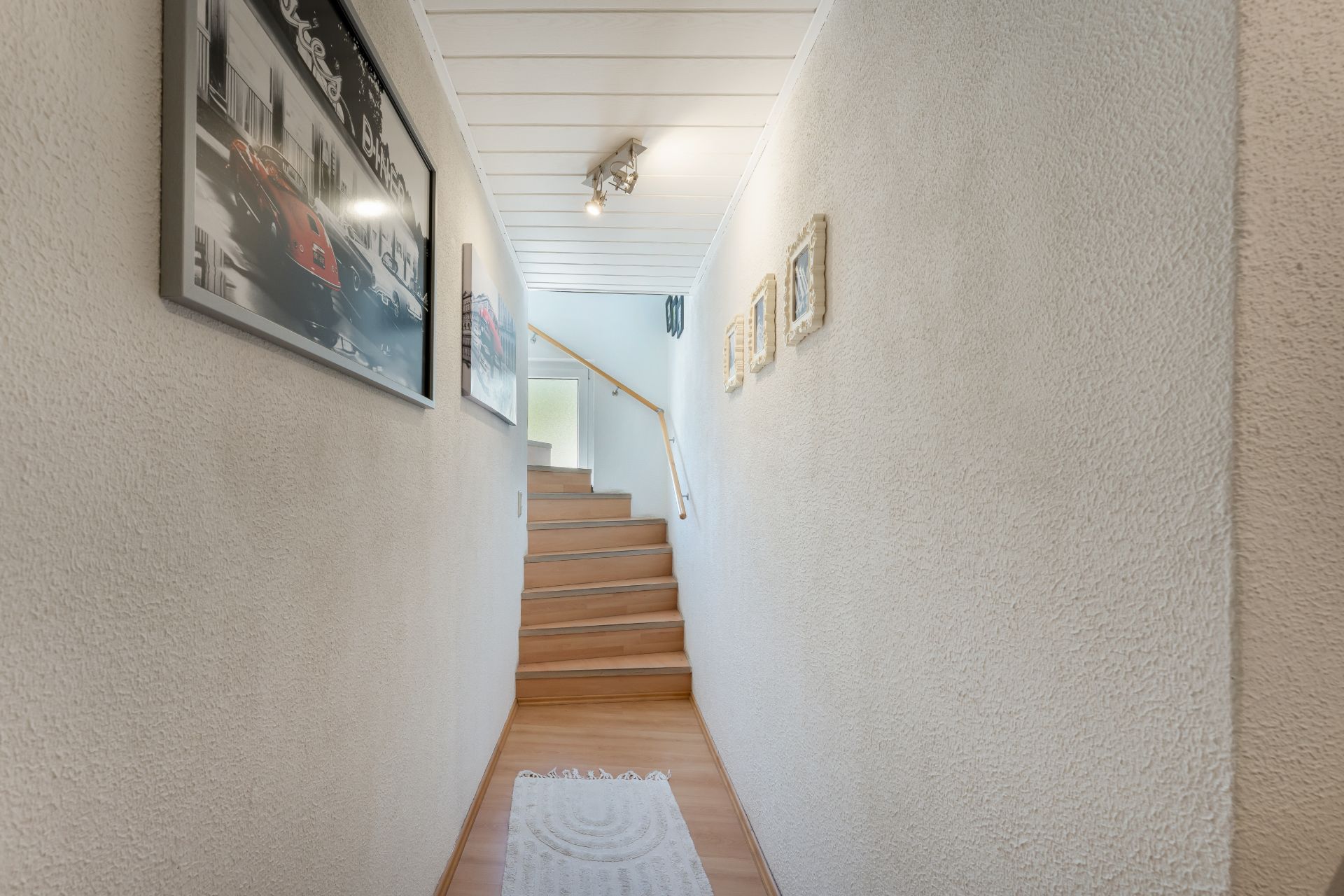 Heller Flur mit Holztreppe, weißen Wänden und gerahmten Bildern an den Wänden.