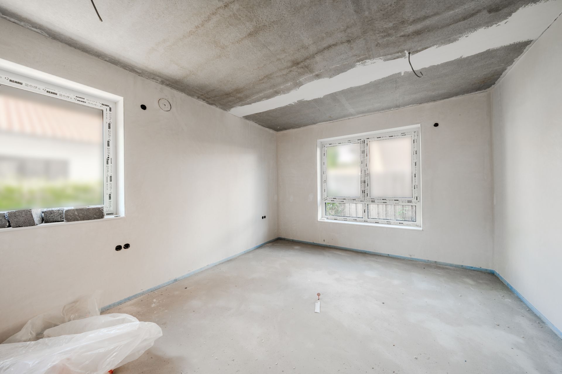 Leerer Raum im Bau mit zwei Fenstern, unverputzten Wänden und Decke.