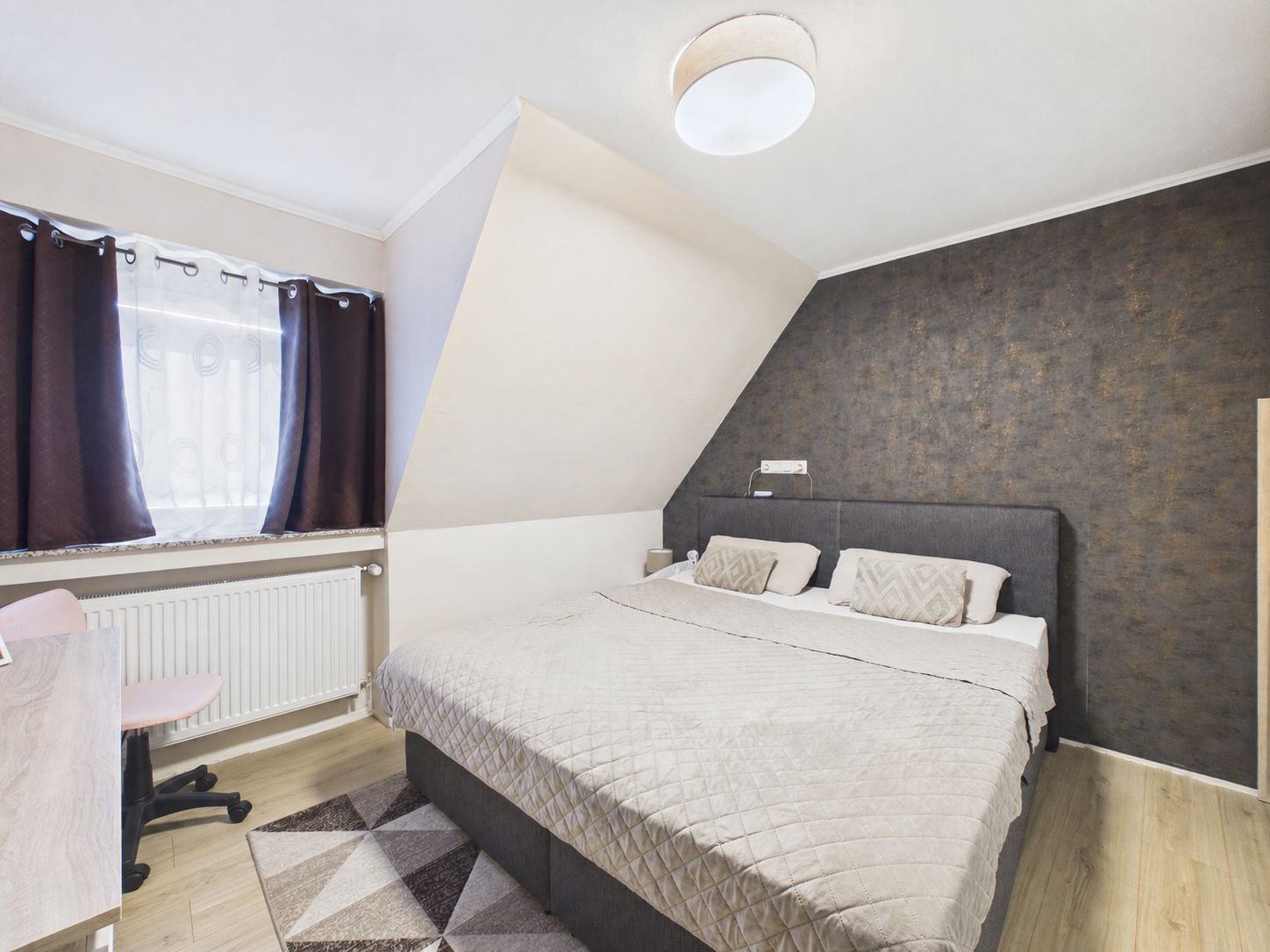 Modernes Schlafzimmer mit Doppelbett, Schreibtisch, Stuhl und Fenster mit dunklen Vorhängen.